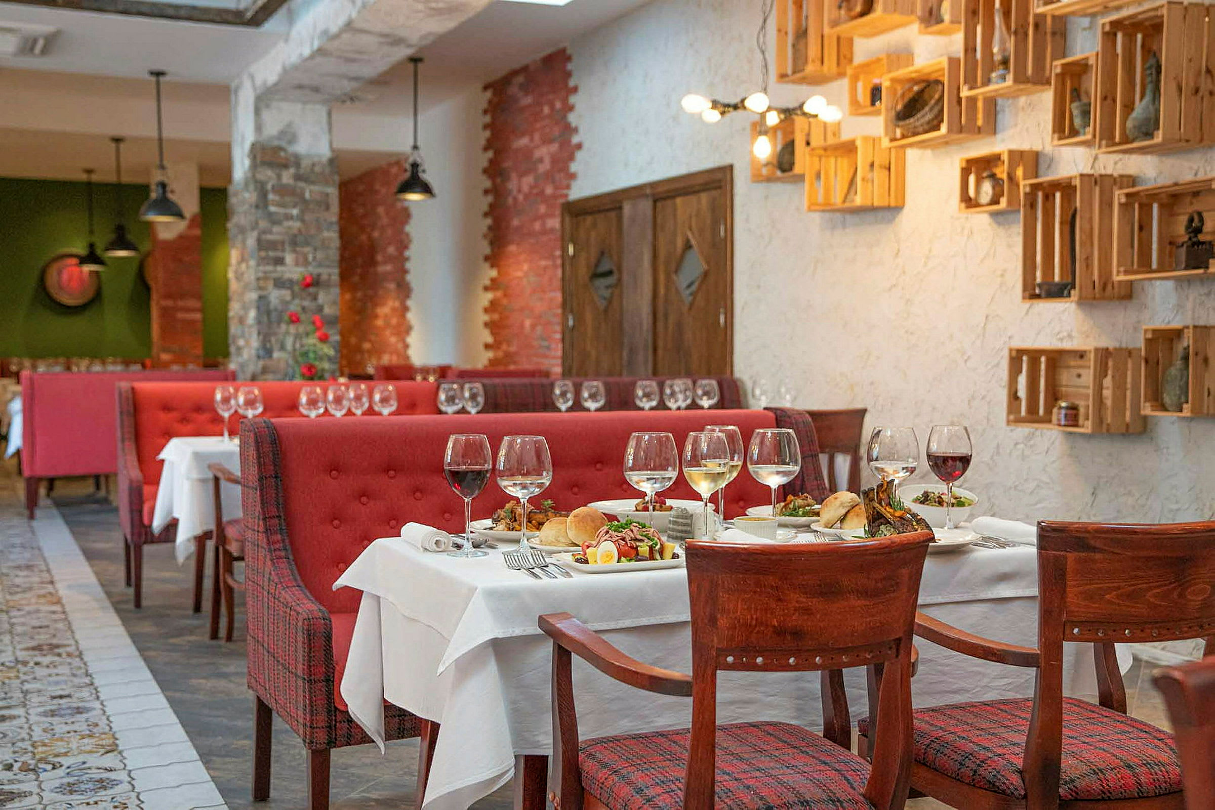 En restaurant med røde sofaer, træstole og dækkede borde med vinglas og madanretninger. (AI-genereret tekst)