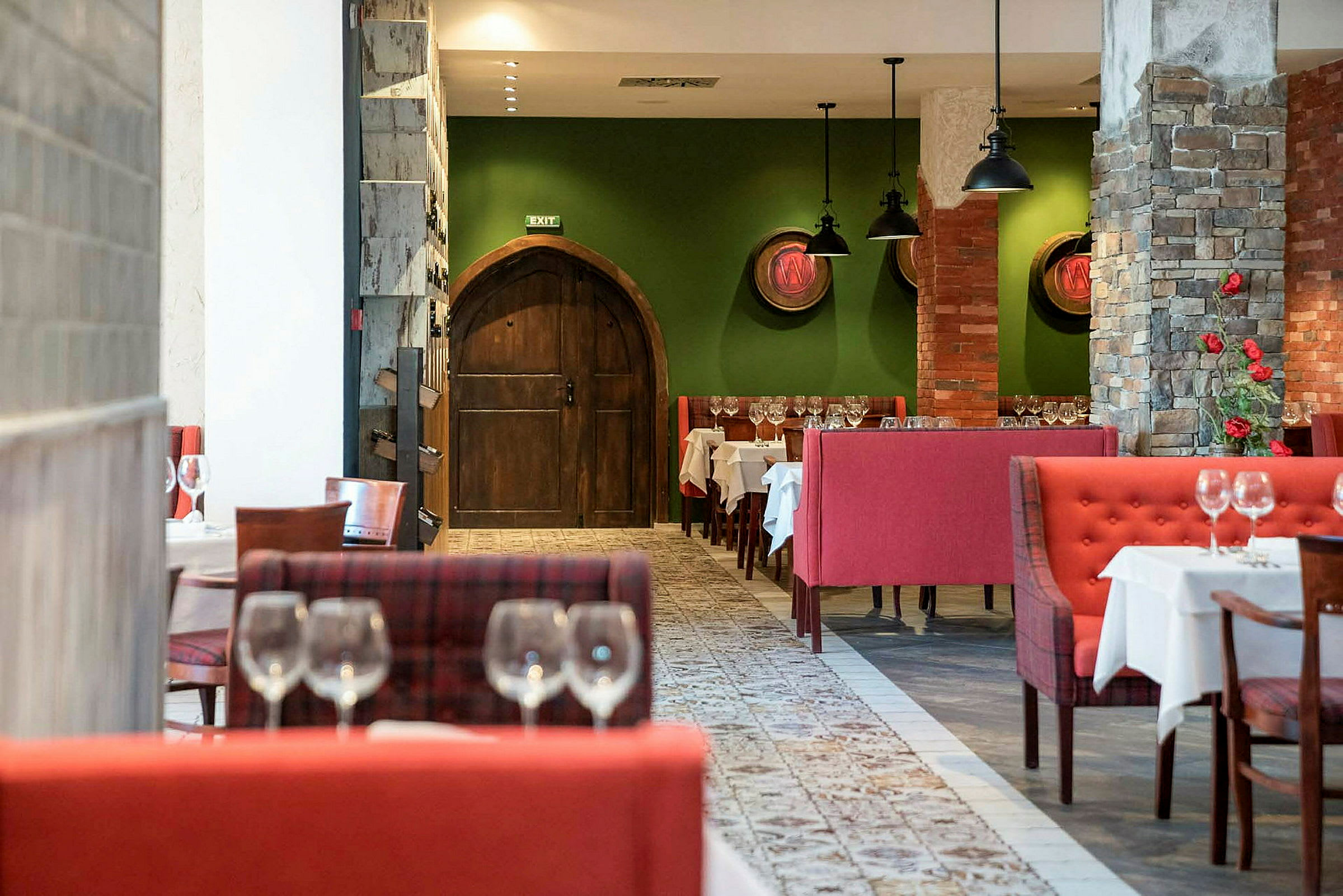 Restaurantinteriør med røde siddegrupper, grønne vægge og gamle trødøre. (AI-genereret tekst)