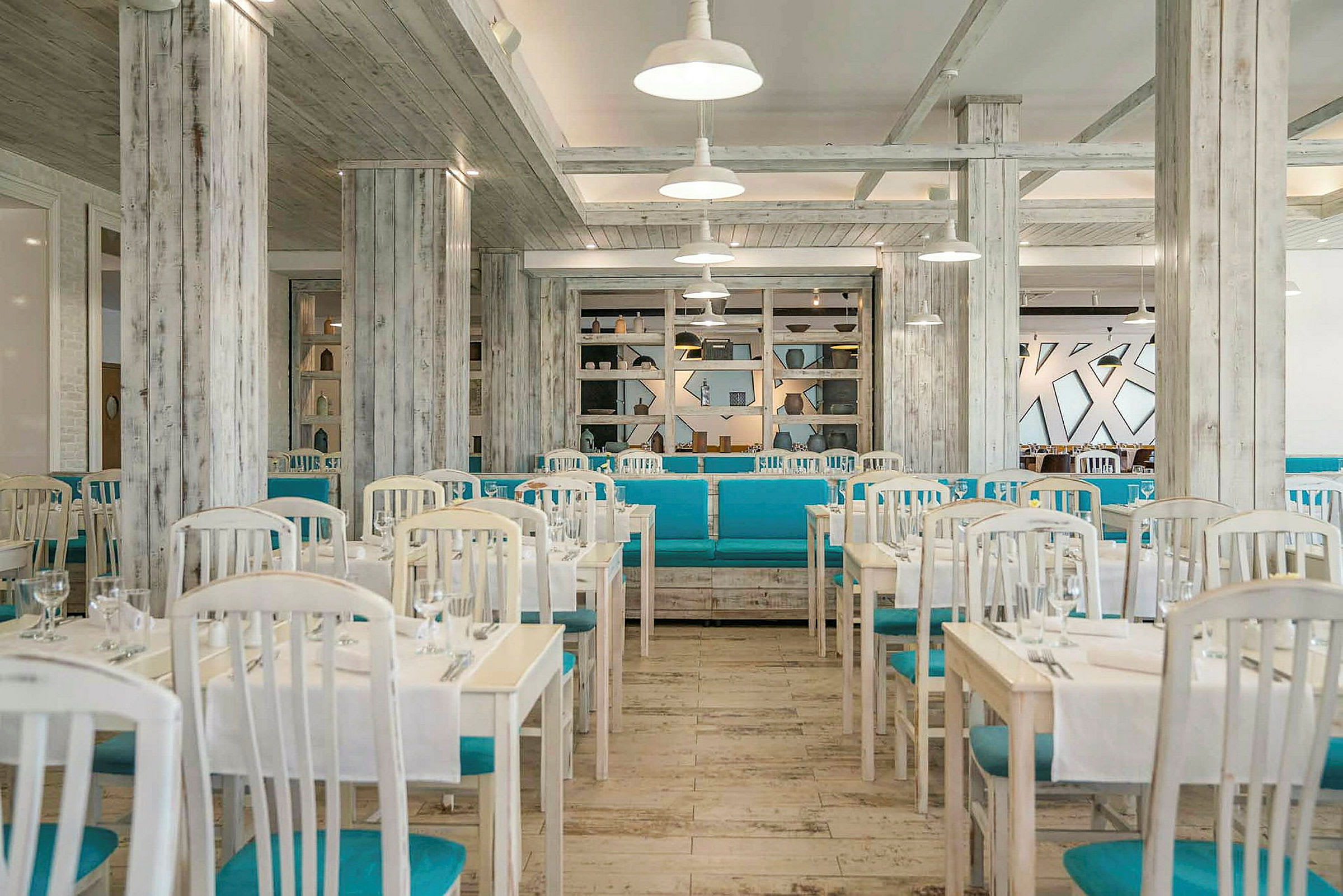 En lys restaurant med hvide borde, blå stole og en stilren indretning. (AI-genereret tekst)
