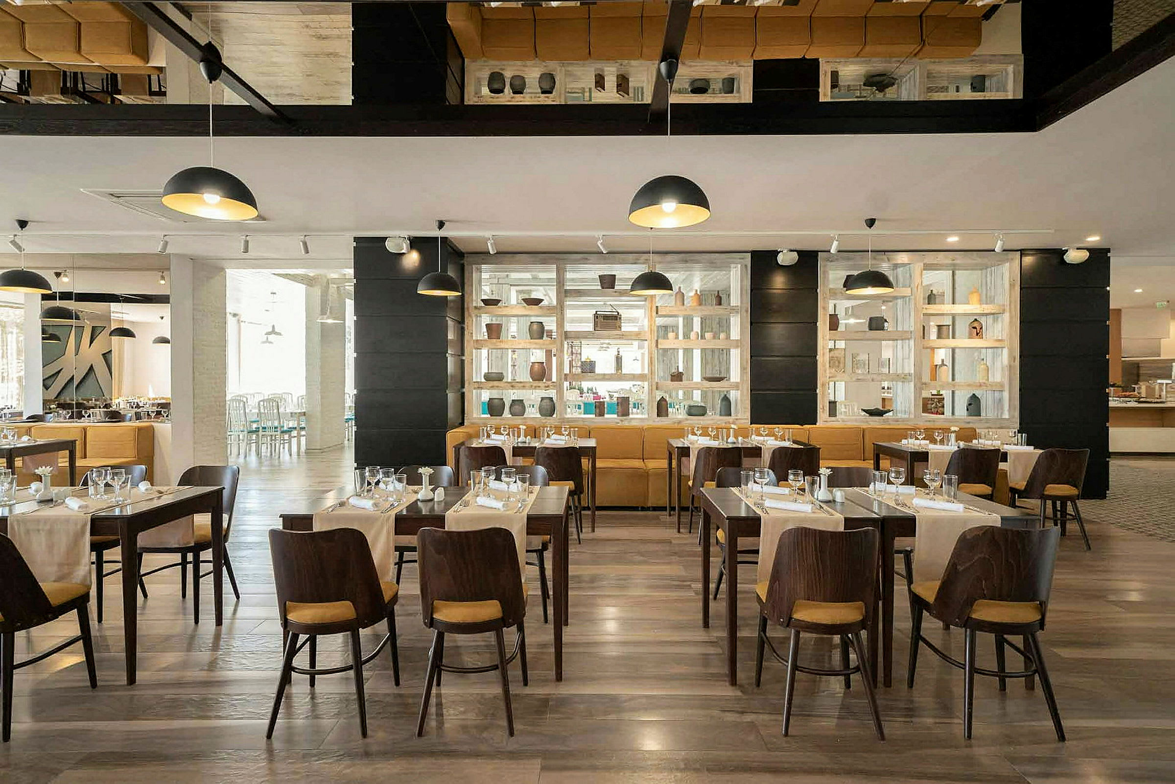 En restaurant med dækkede træborde og stole. Dekorativ hylde ved væggen. (AI-genereret tekst)