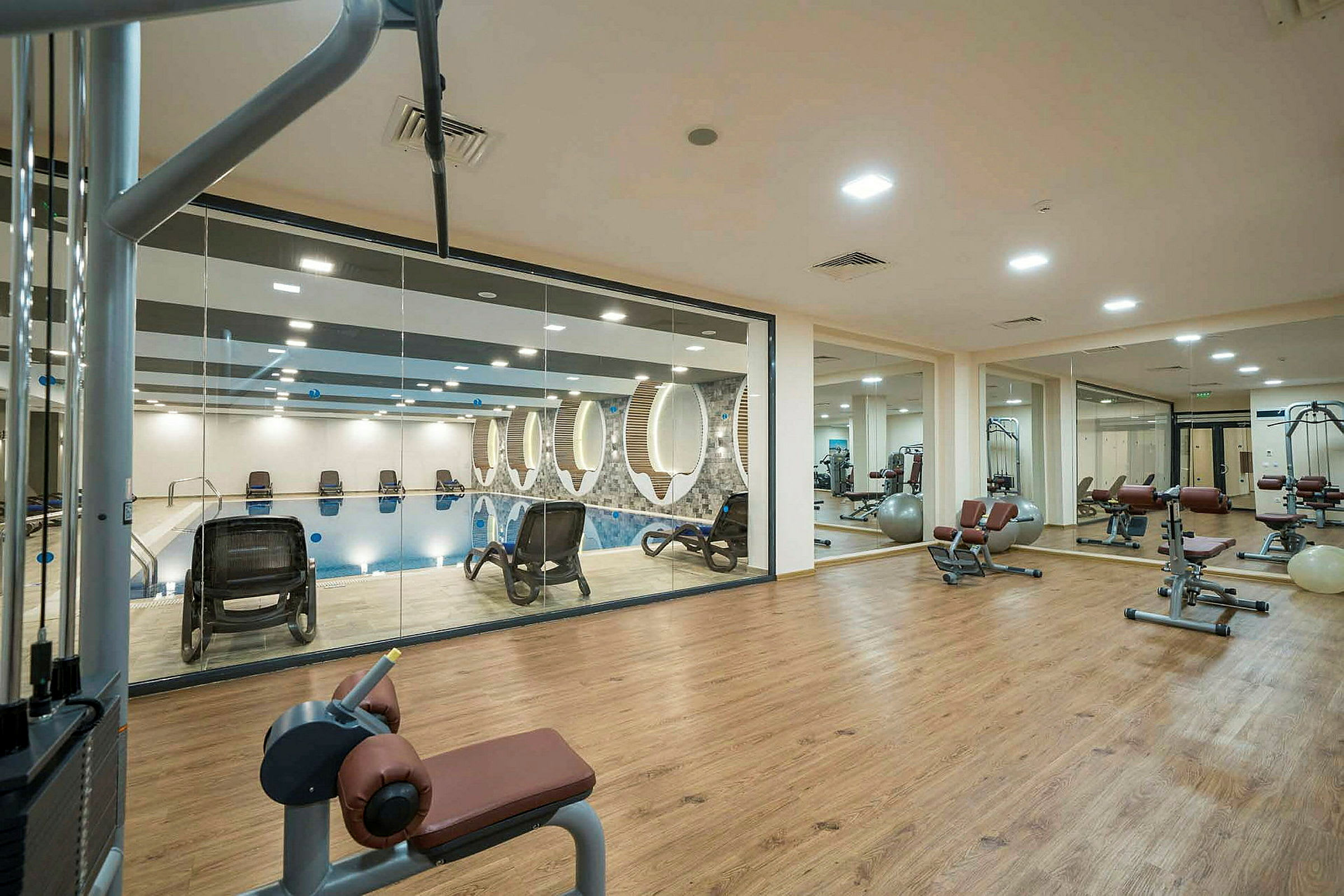 Et fitnesscenter med træningsudstyr og glasvæg mod en pool. (AI-genereret tekst)