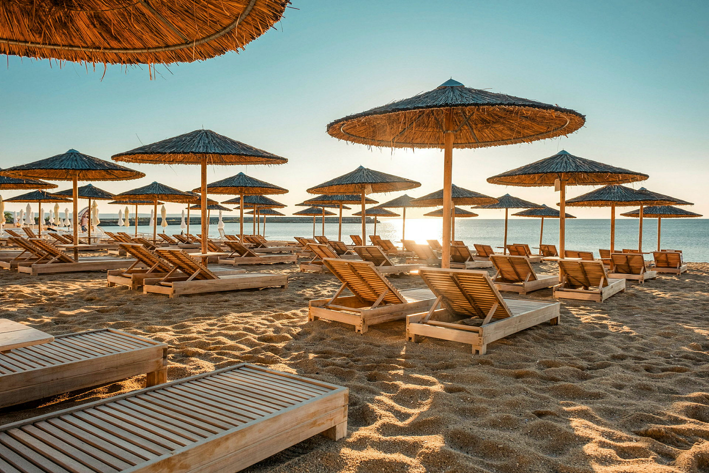 Strand med solvogne og parasoller af halm ved vandet. (AI-genereret tekst)