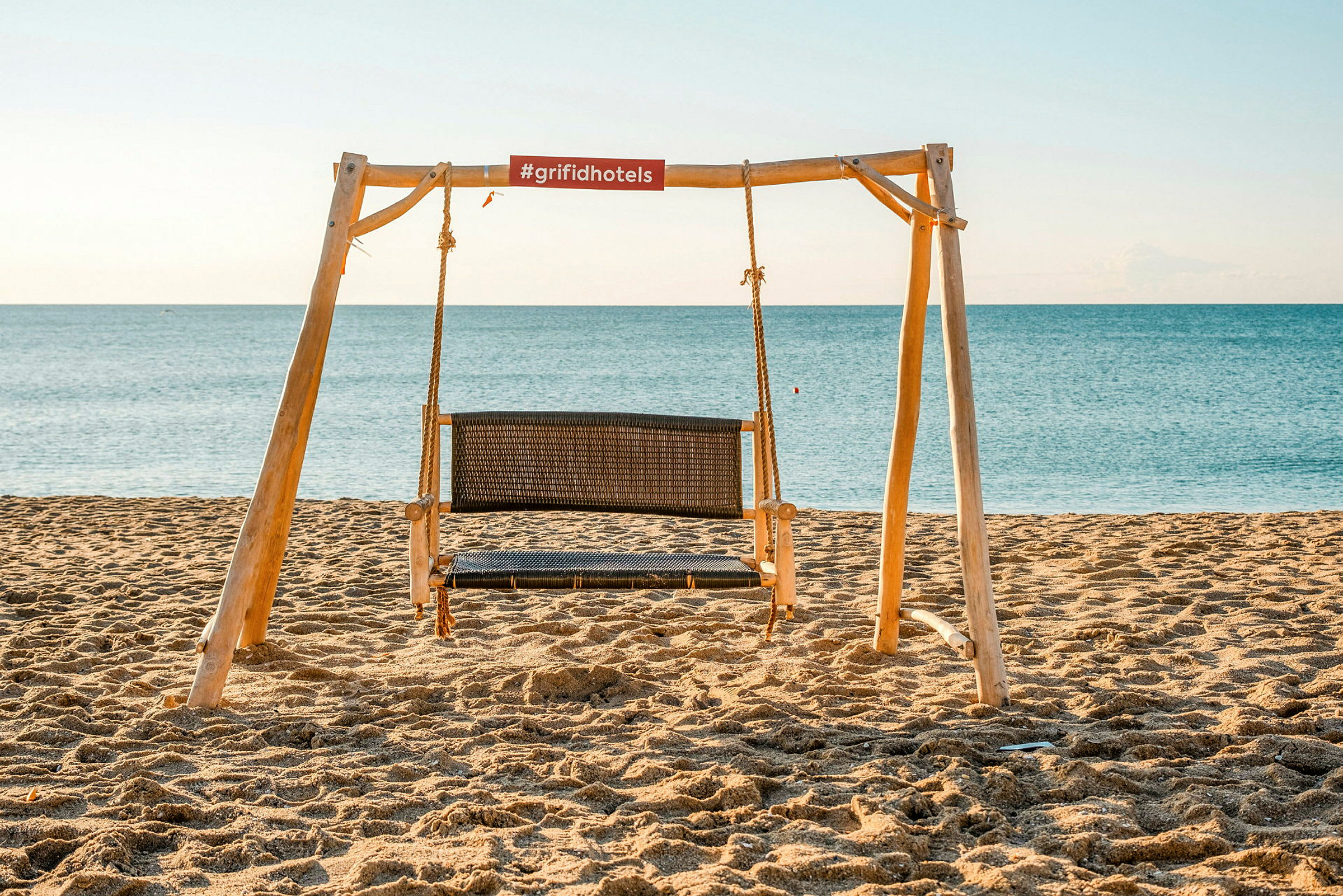En trægyngestativ med en siddegyng på en sandstrand ved havet. (AI-genereret tekst)