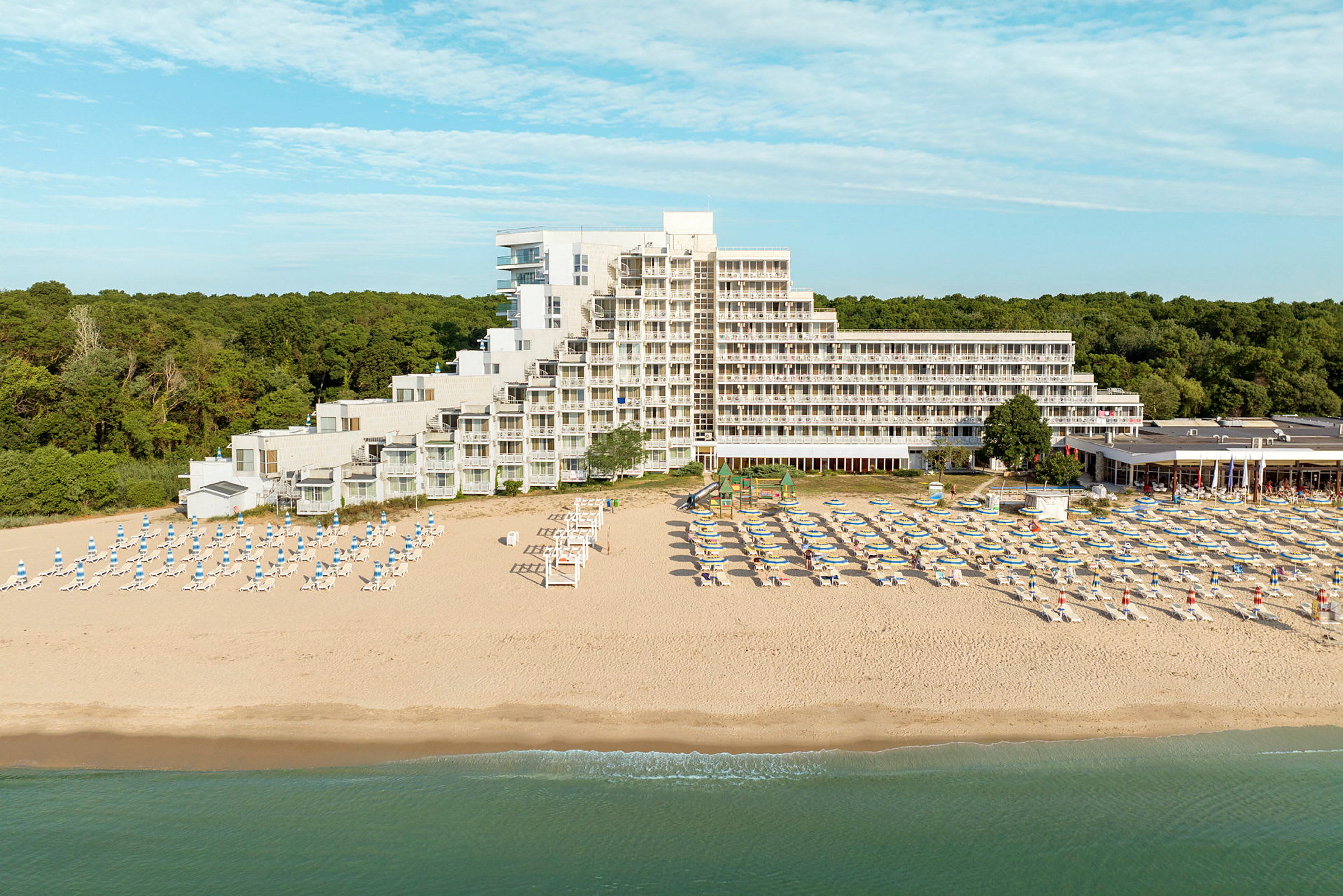 En strand med liggestole og parasoller foran et hotel ved kysten. (AI-genereret tekst)