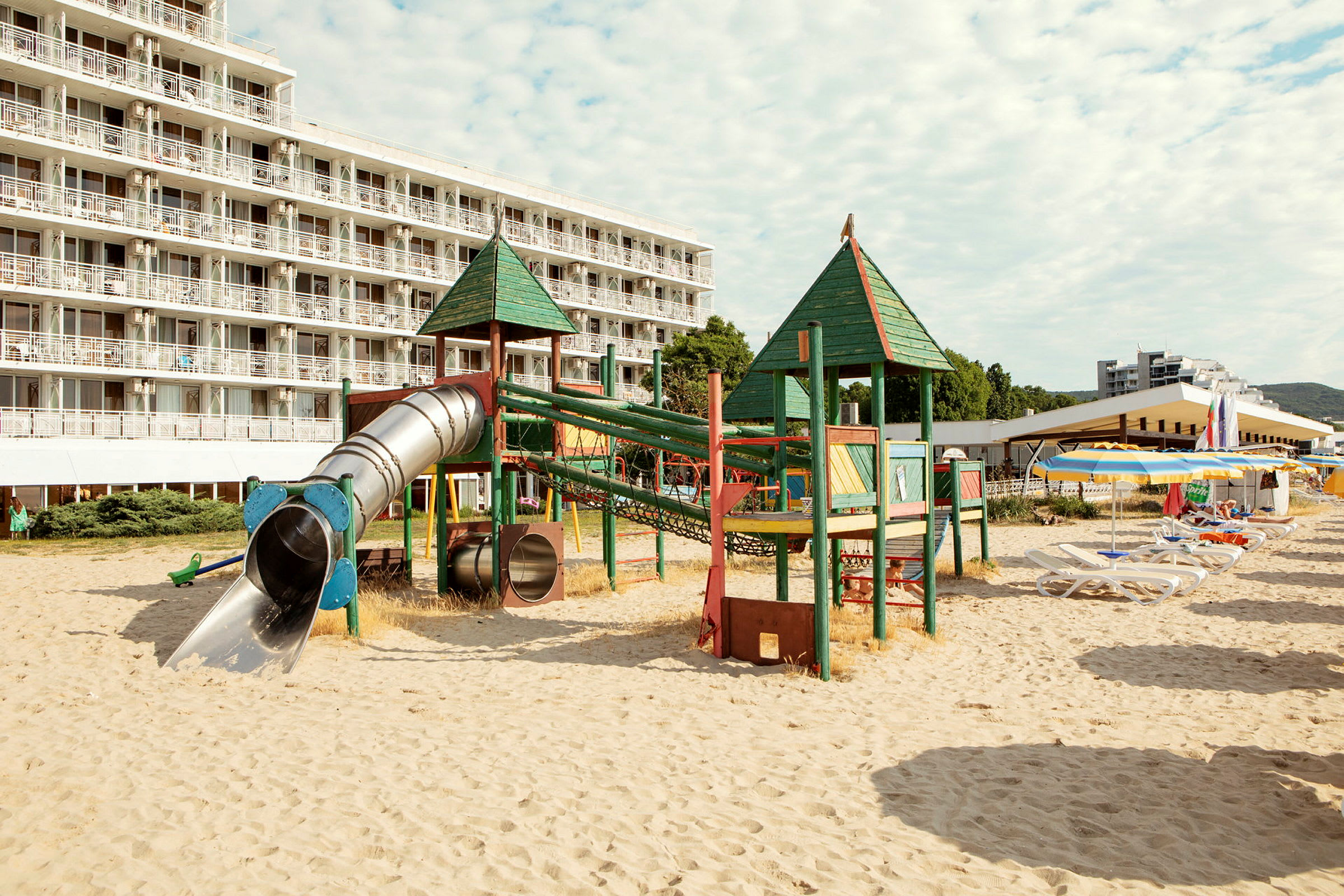 Legeplads med rutsjebaner på sandstrand foran hotel. (AI-genereret tekst)