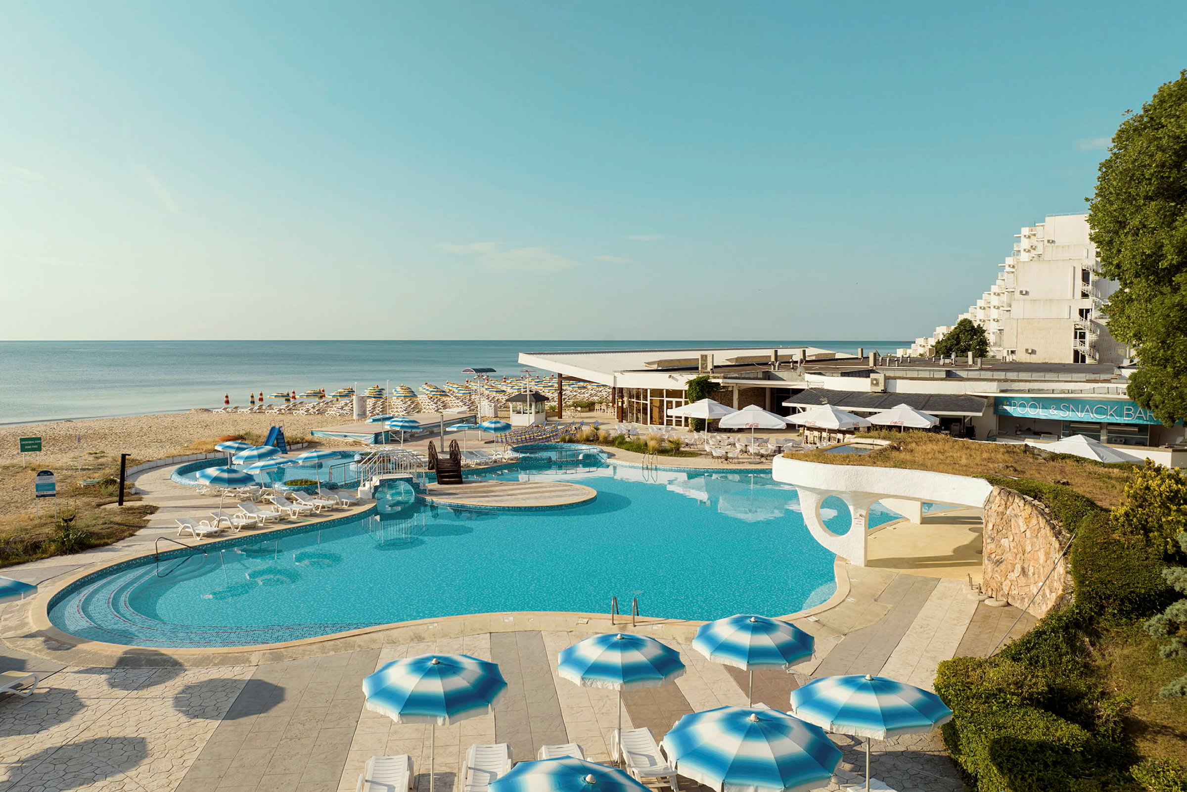 Hotel med poolområde og parasoller ved stranden. (AI-genereret tekst)