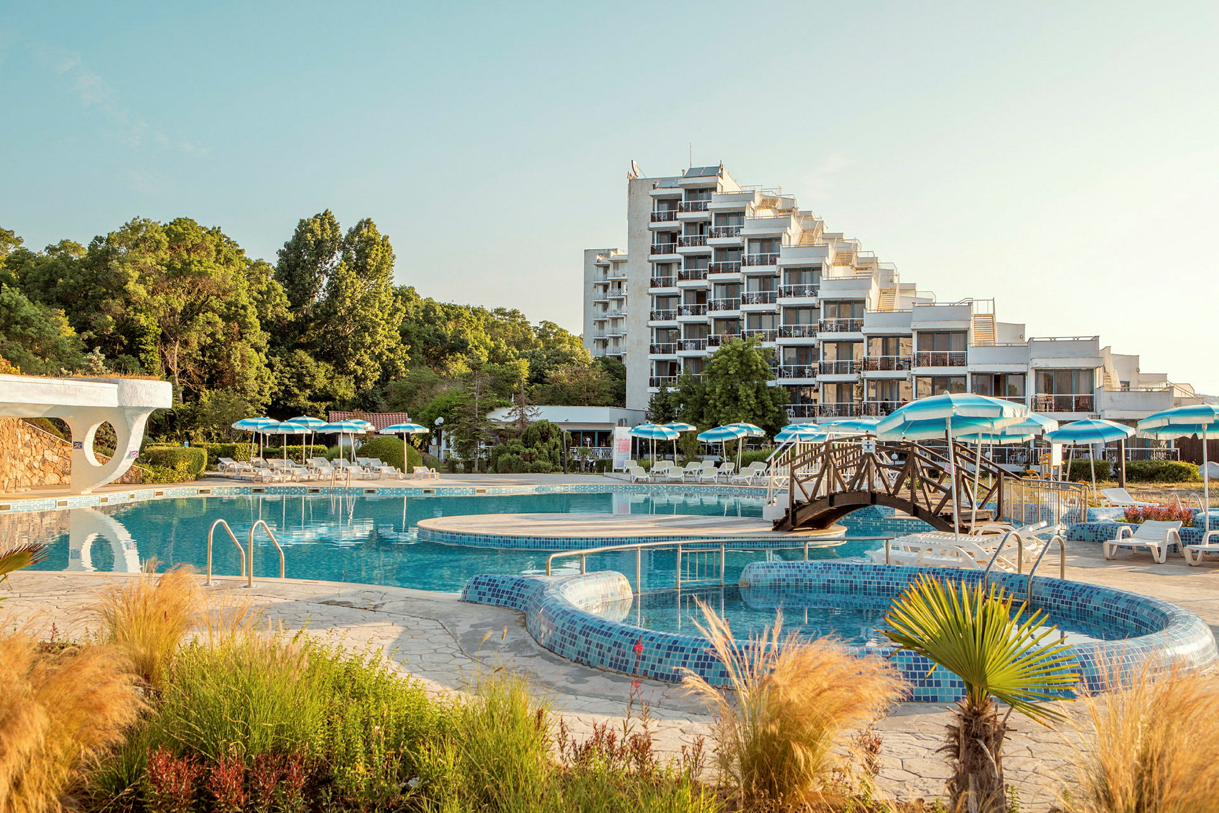 Hotel med et stort poolområde og parasoller blandt grønt. (AI-genereret tekst)