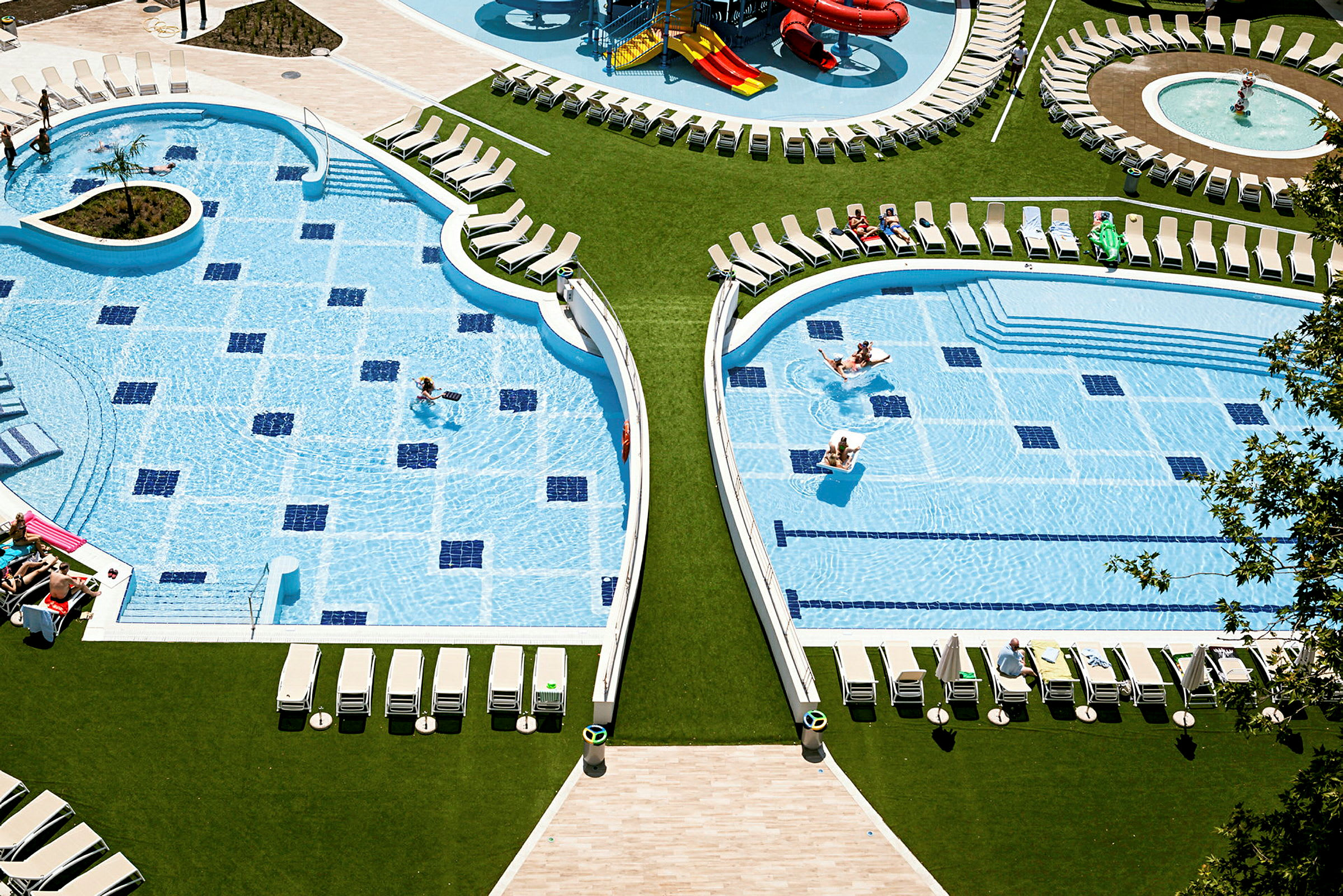 To swimmingpools omgivet af liggestole og grønt område. (AI-genereret tekst)
