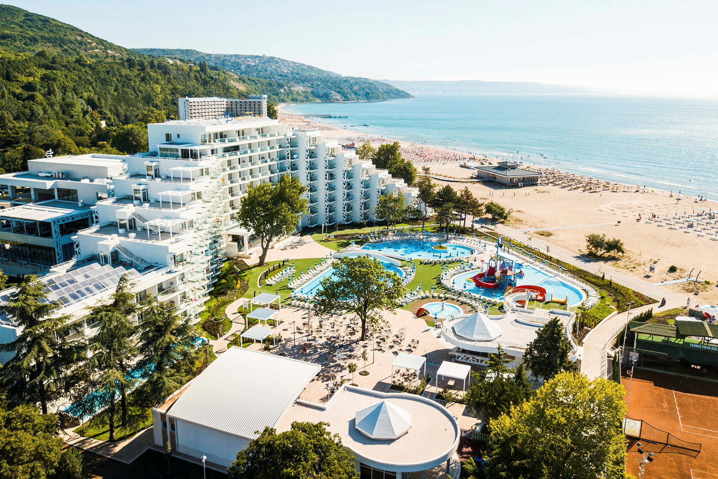 Billede af et hotelkompleks med pools og legeplads tæt på stranden. (AI-genereret tekst)