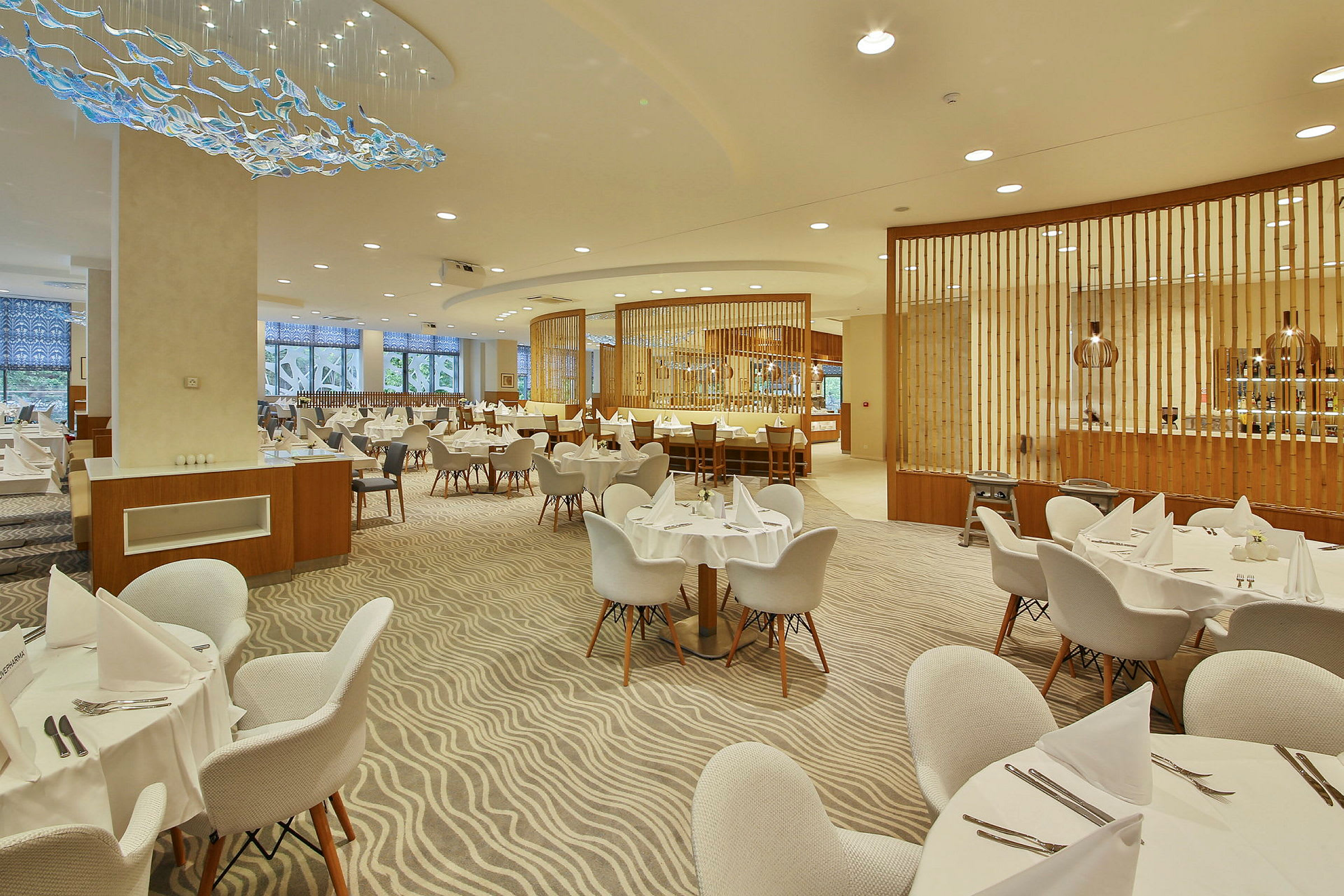 En stor og velbelyst restaurant med dækkede runde borde og moderne møbler. (AI-genereret tekst)