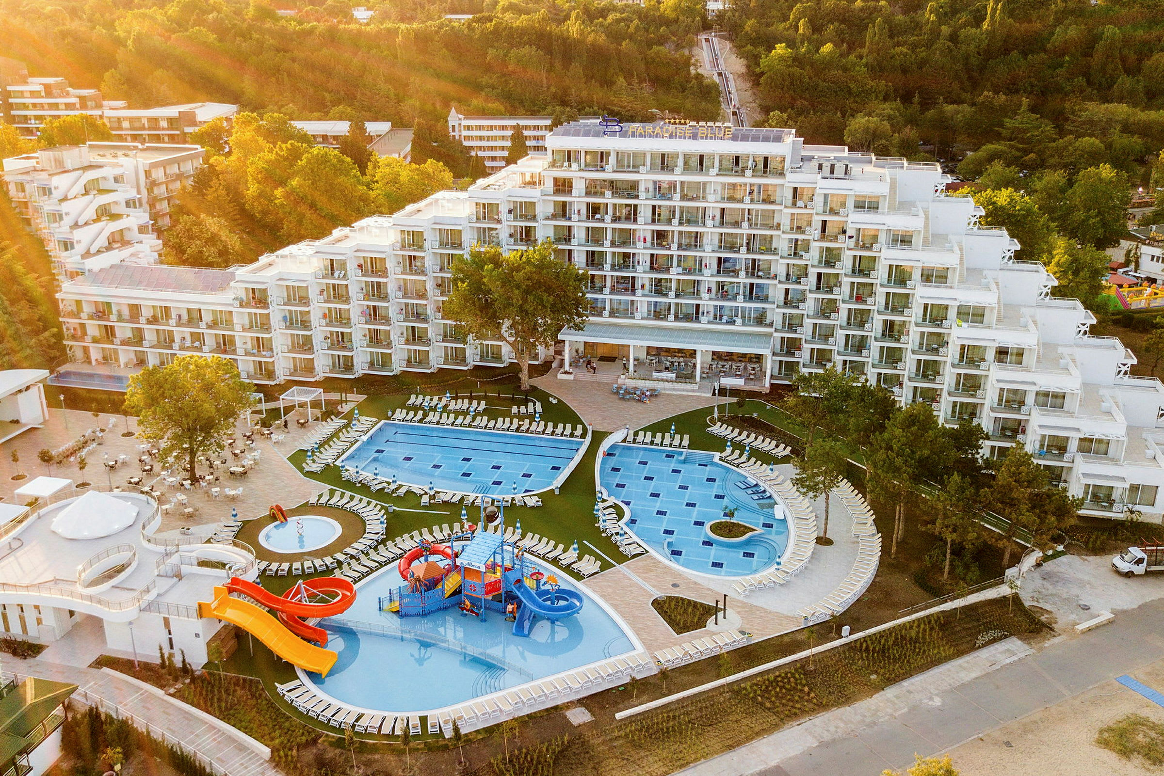 Hotel med poolområde, vandrutsjebaner og grønne omgivelser. (AI-genereret tekst)