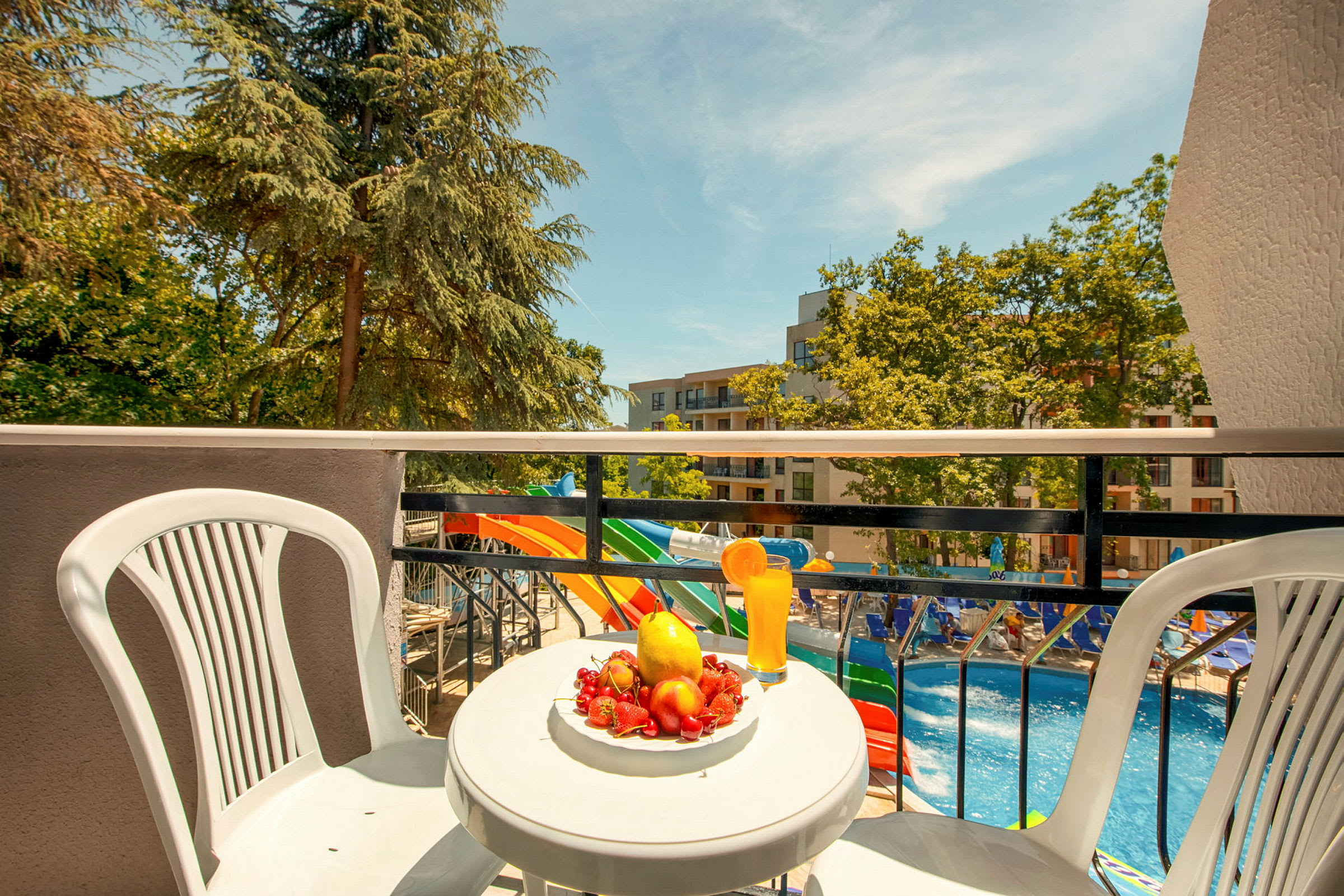 Et bord med frugt og en drik på en balkon med udsigt til poolen og vandrutsjebaner. (AI-genereret tekst)
