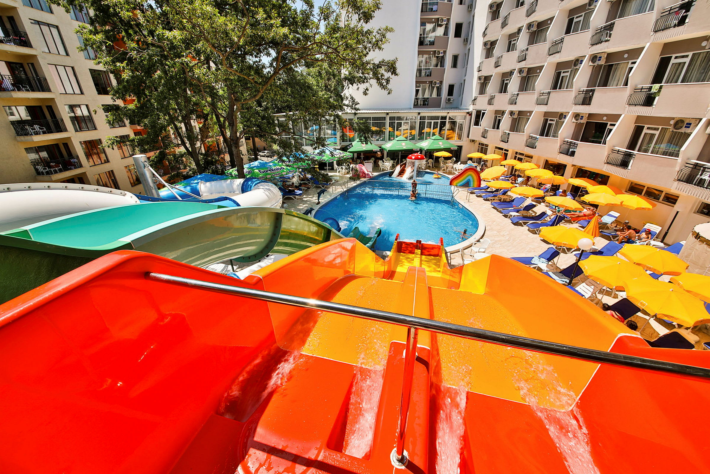 En udendørs pool med vandrutsjebane, liggestole og parasoller ved et hotelområde. (AI-genereret tekst)