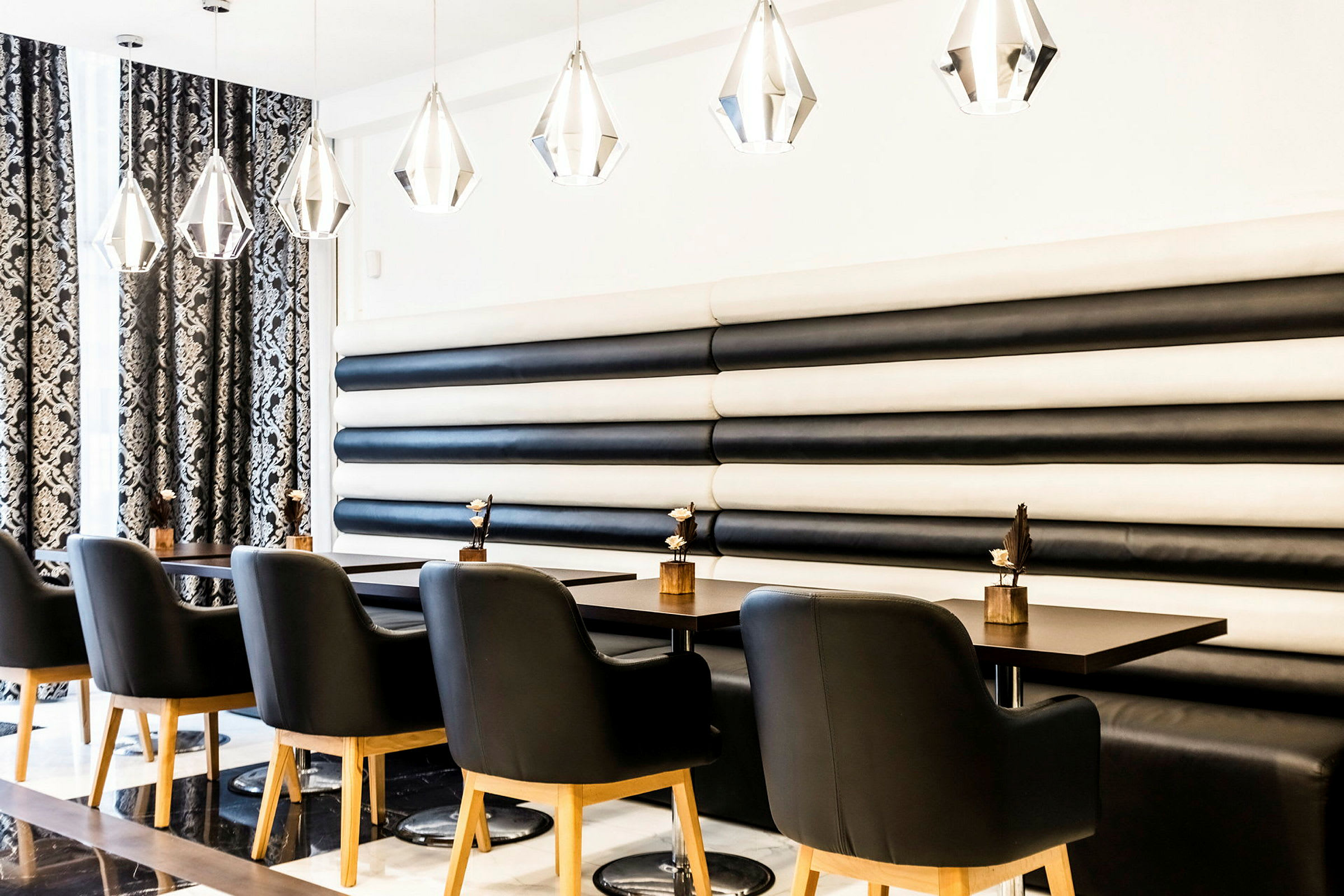 En moderne restaurant med sort og hvidt interiør. Sorte stole med træben står ved borde med dekorative genstande. (AI-genereret tekst)