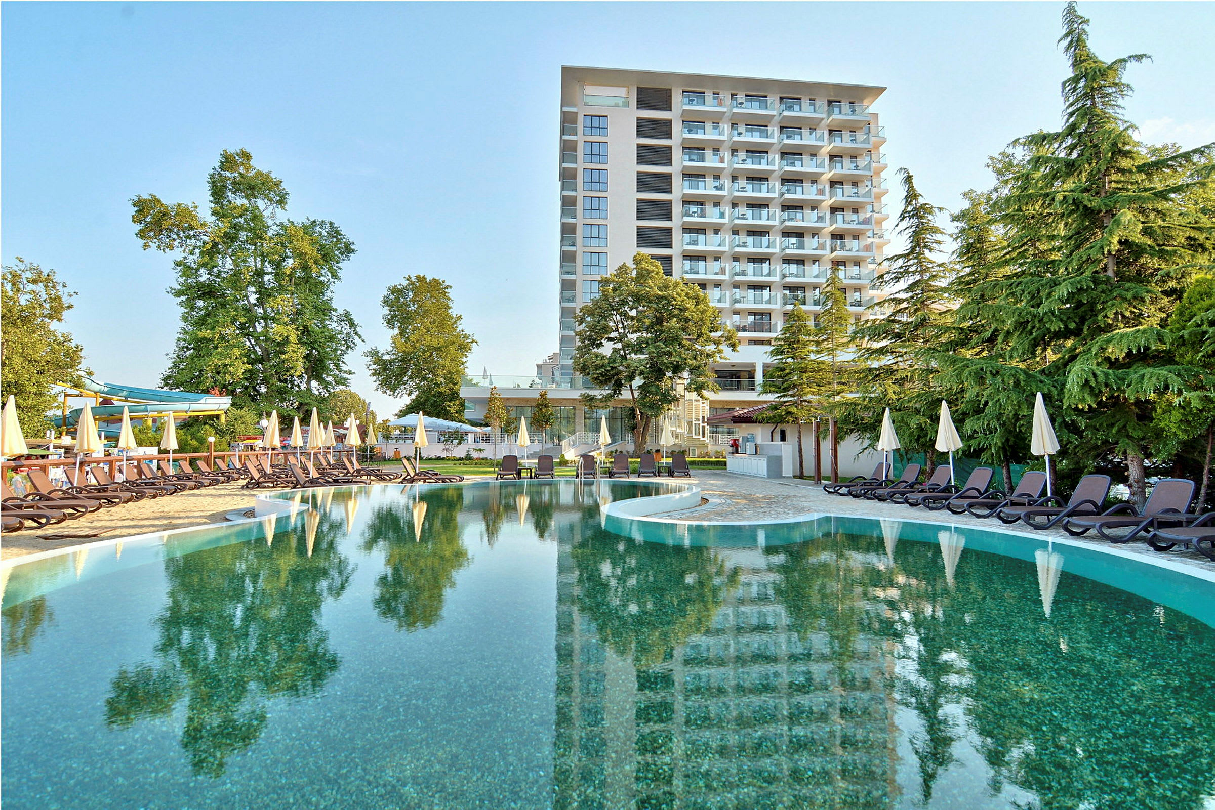 Hotel med turkis vand ved poolområdet, omgivet af solsenge og grønne træer. (AI-genereret tekst)