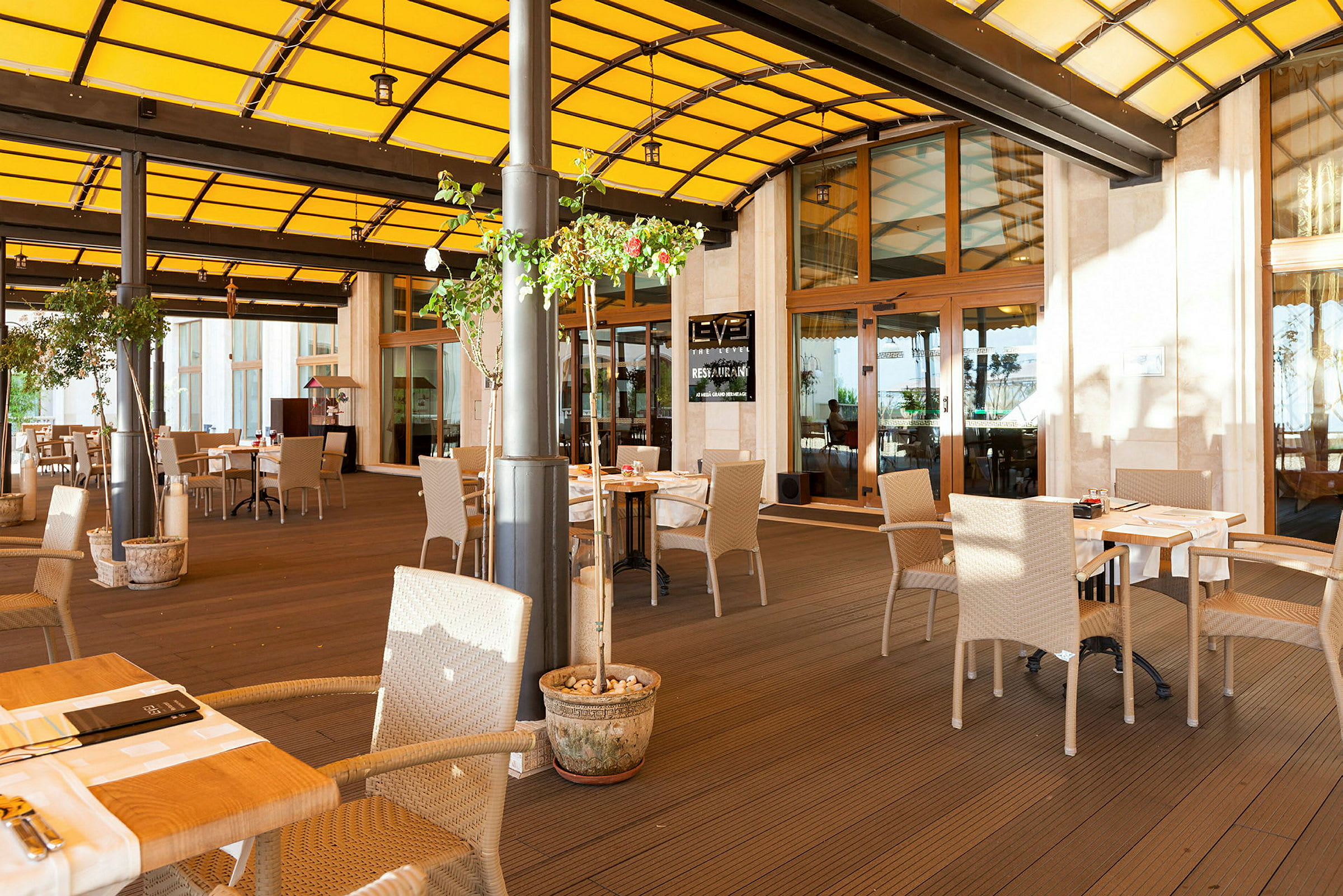 En udendørs terrasse med siddepladser og borde under et gult tag. (AI-genereret tekst)