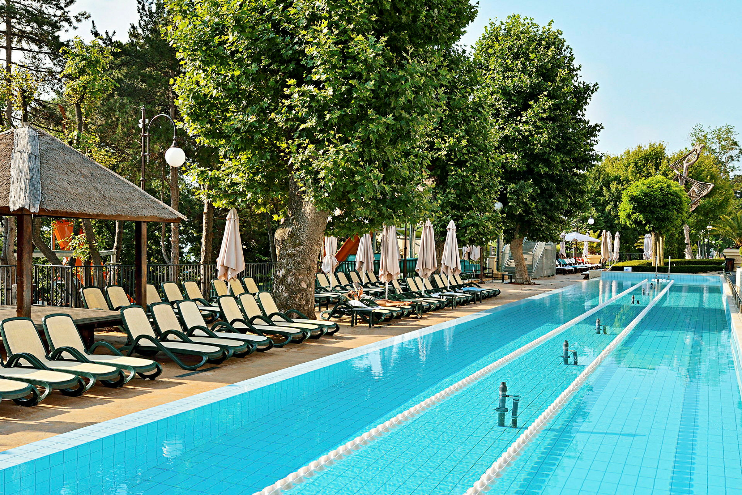 Poolområde med liggestole og parasoller ved siden af en lang rektangulær pool. (AI-genereret tekst)