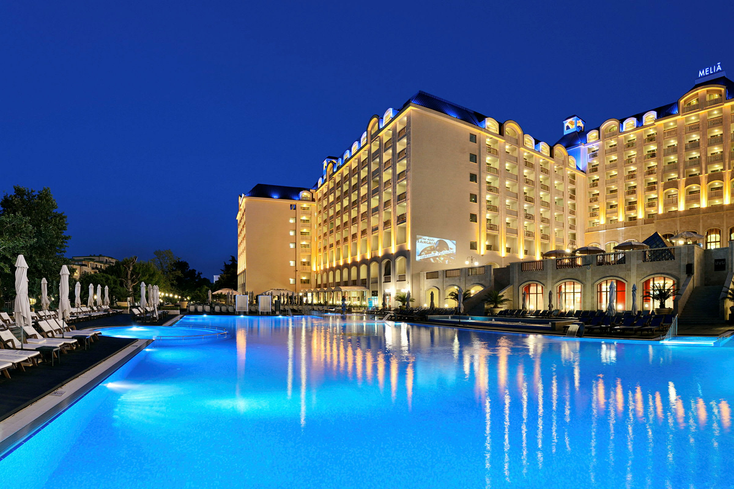 Hotelbygning ved en oplyst pool om aftenen. (AI-genereret tekst)