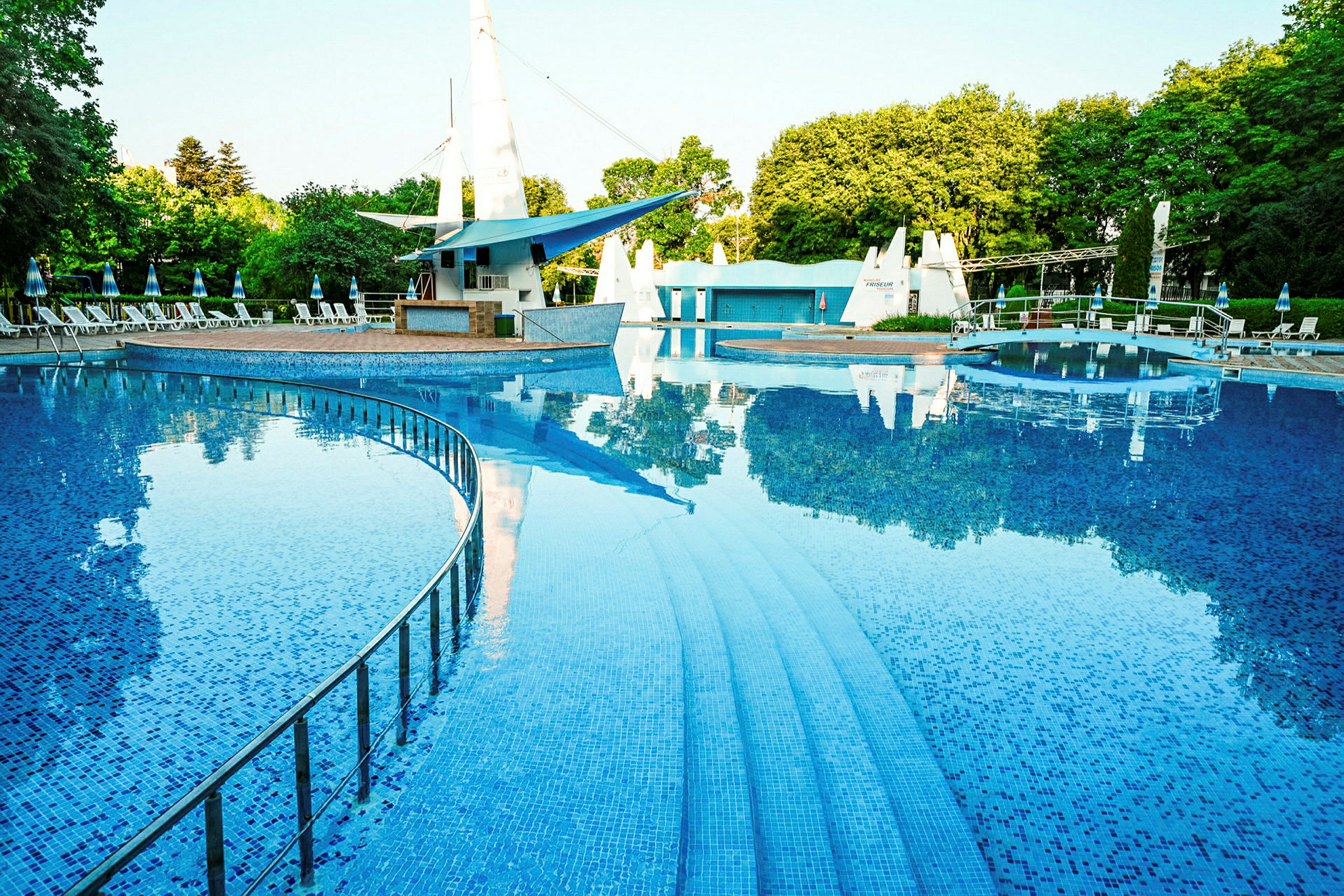 Udendørs pool med trapper og omgivende liggestole under parasoller. (AI-genereret tekst)