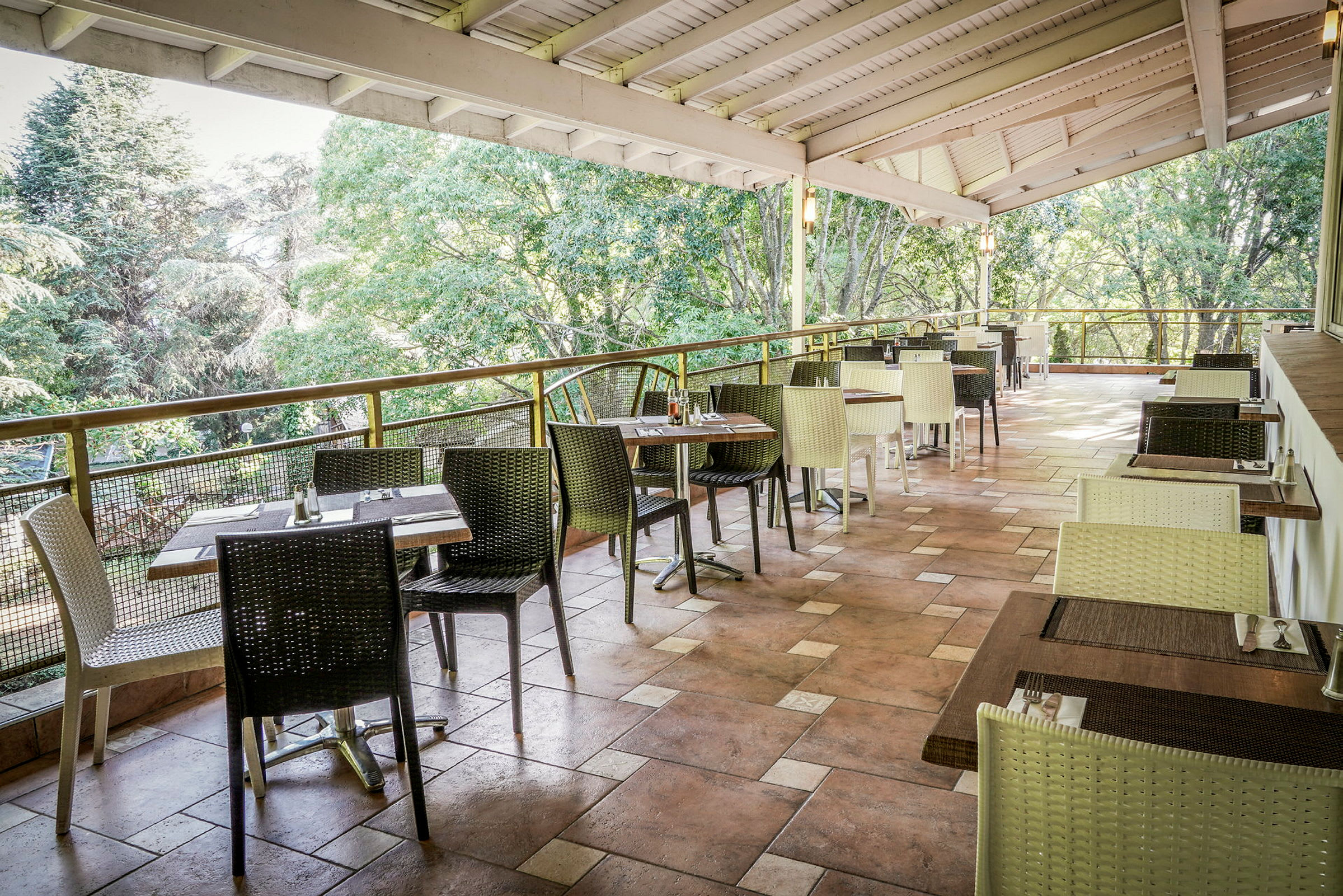 En åben restaurantterrasse med borde og stole, omgivet af frodige træer. (AI-genereret tekst)