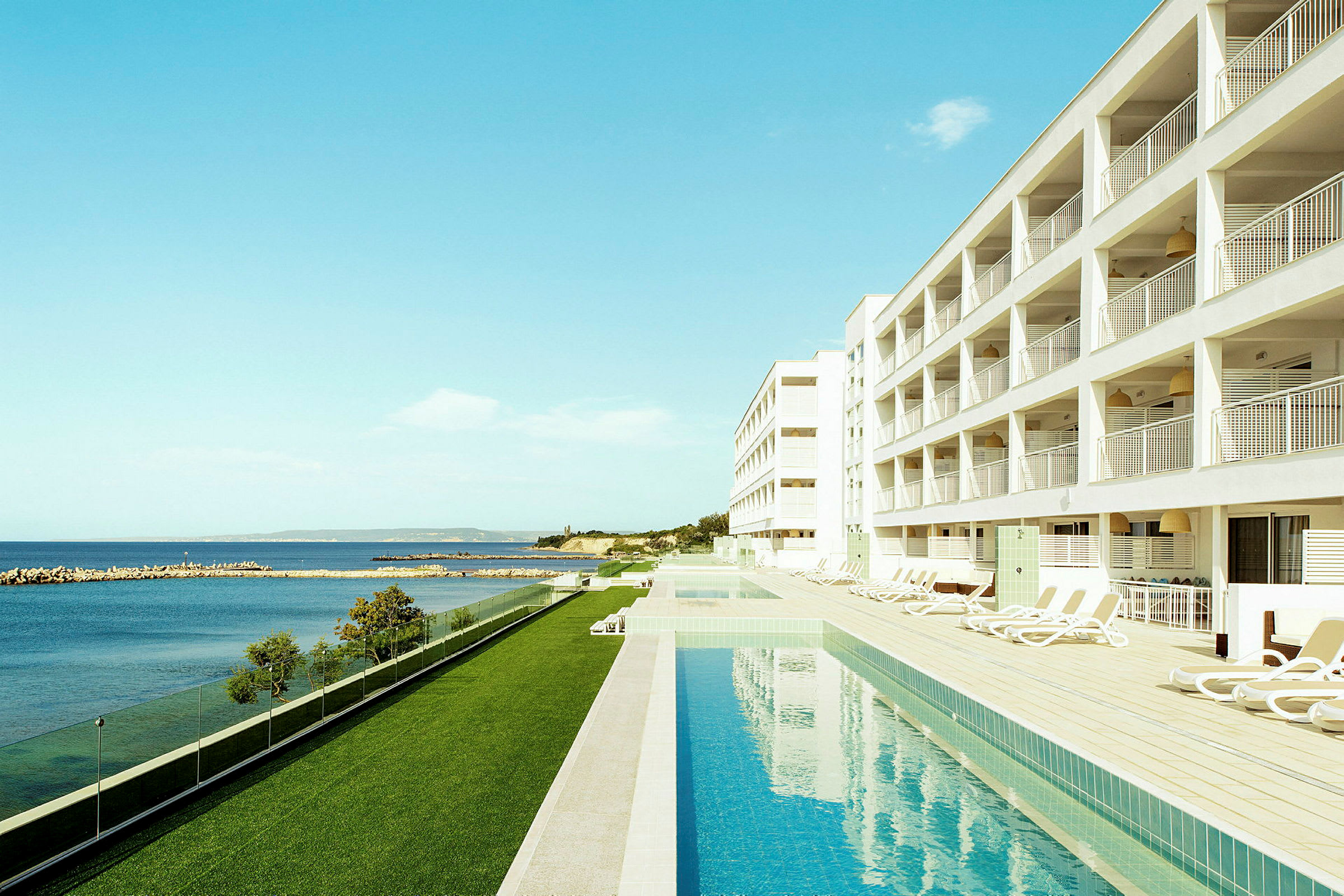 Hotel med pool ved havet og liggestole ved siden af. (AI-genereret tekst)