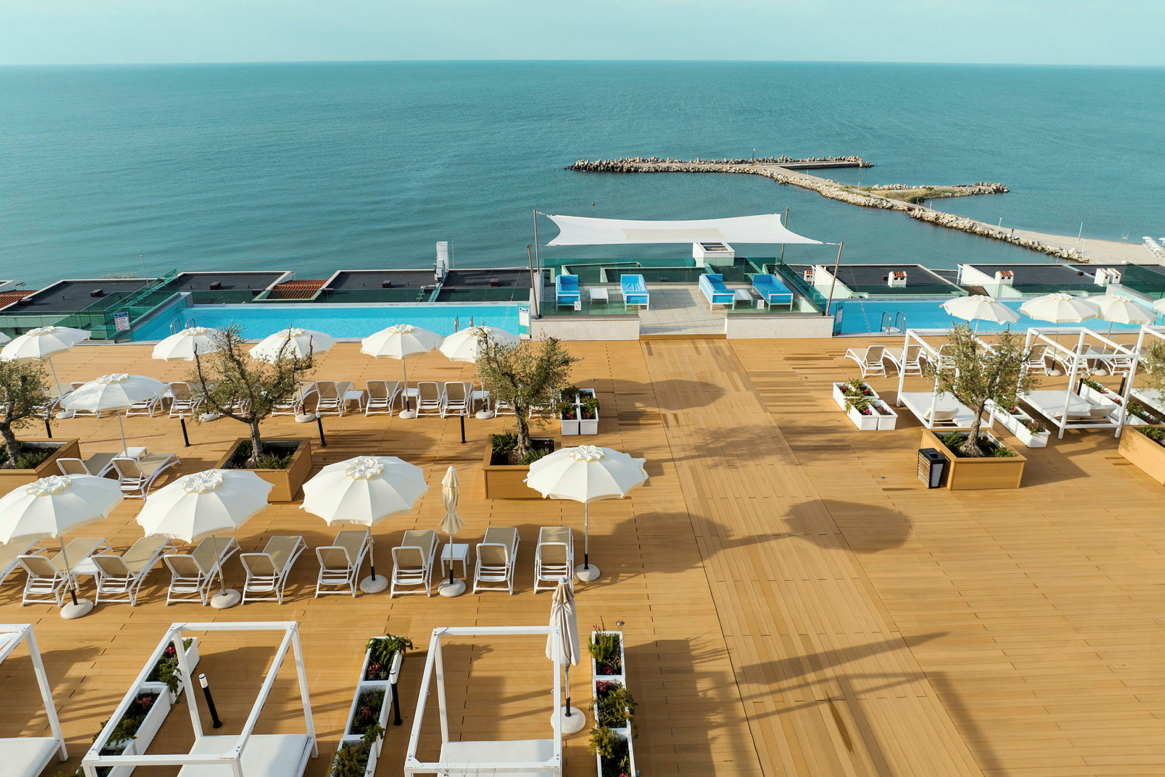 Liggestole og parasoller på en terrasse med udsigt over havet og swimmingpools. (AI-genereret tekst)