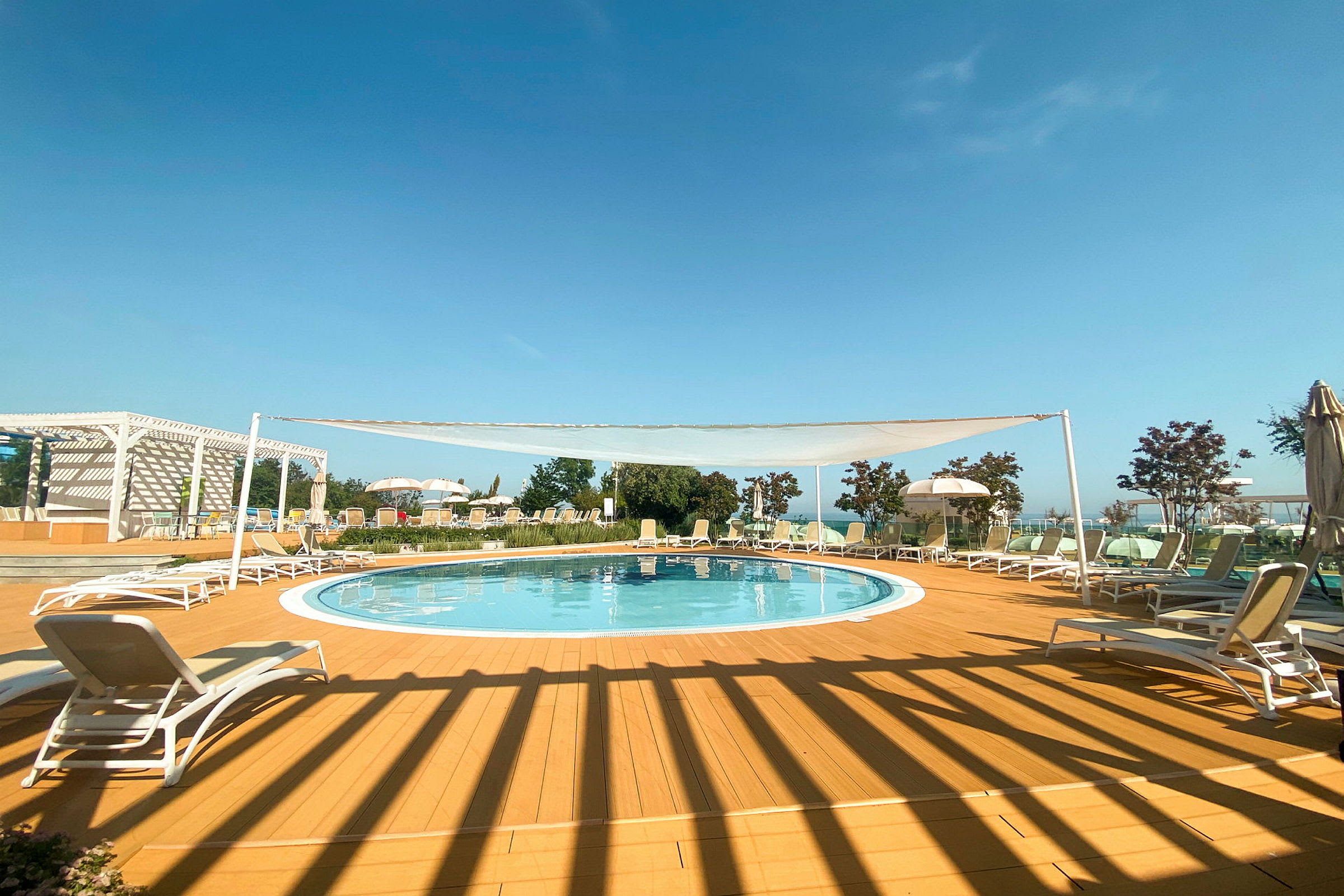 Udendørs pool med liggestole og afslapningsområde under en klar himmel. (AI-genereret tekst)