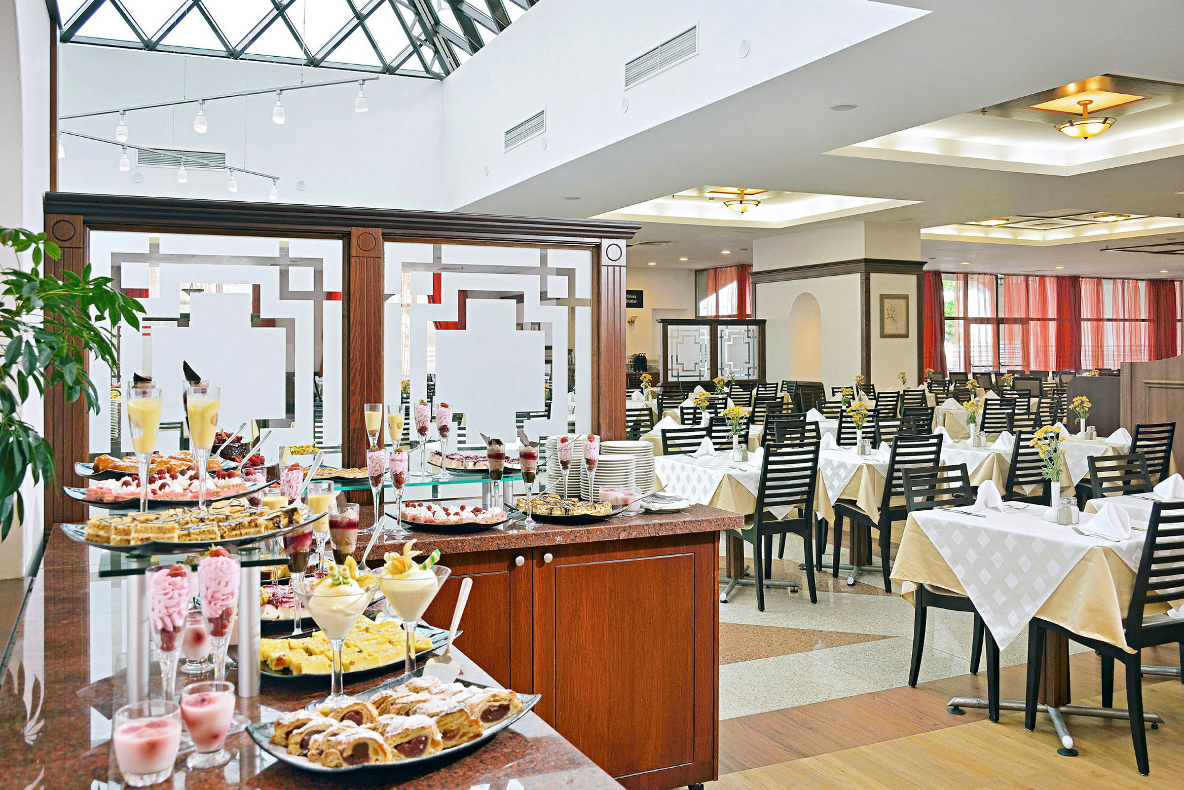 Buffetbord med desserter i en lys restaurant med opdækkede borde. (AI-genereret tekst)