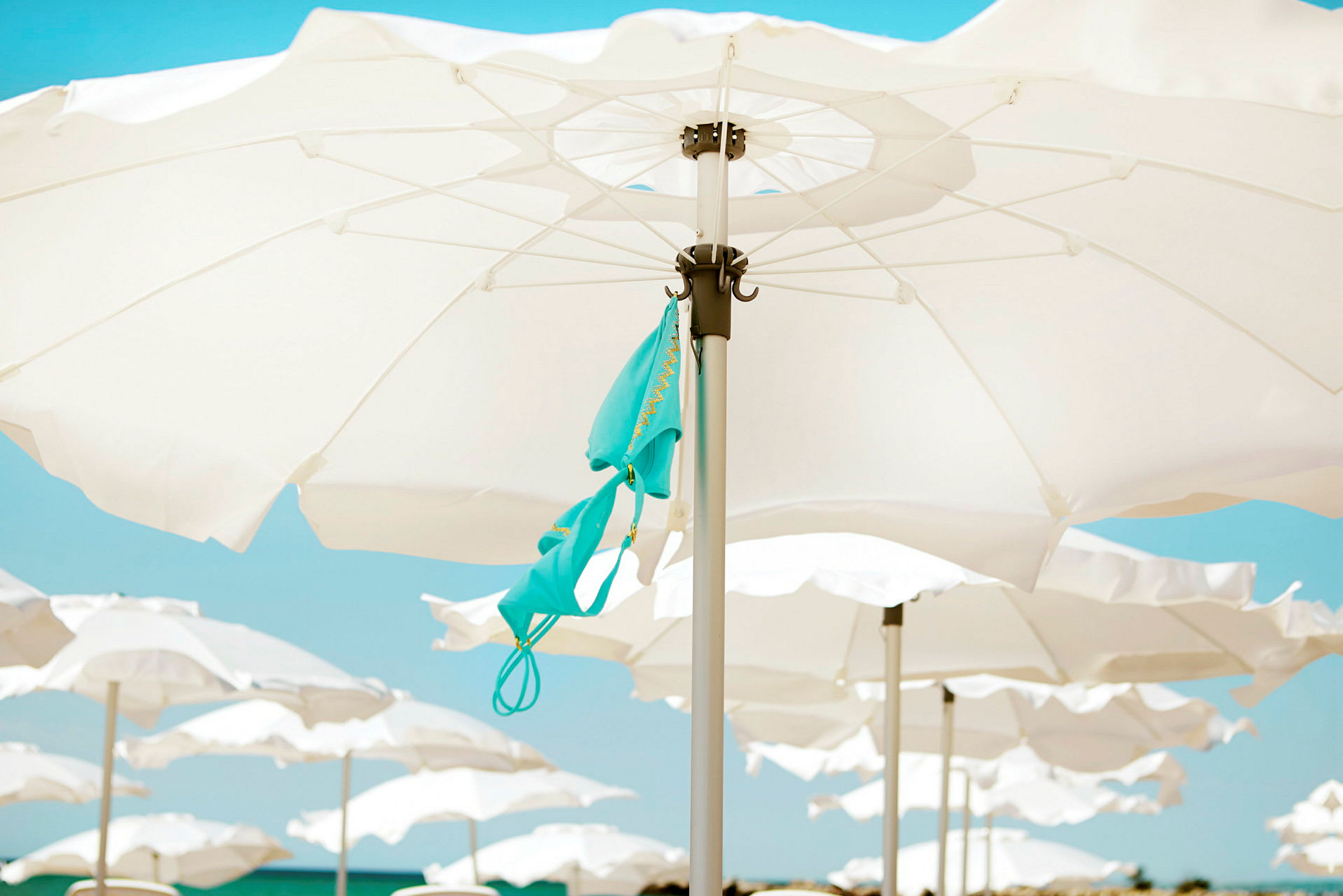 Paraplyer på en strand med en turkis bikinioverdel hængende fra en af paraplyerne. (AI-genereret tekst)