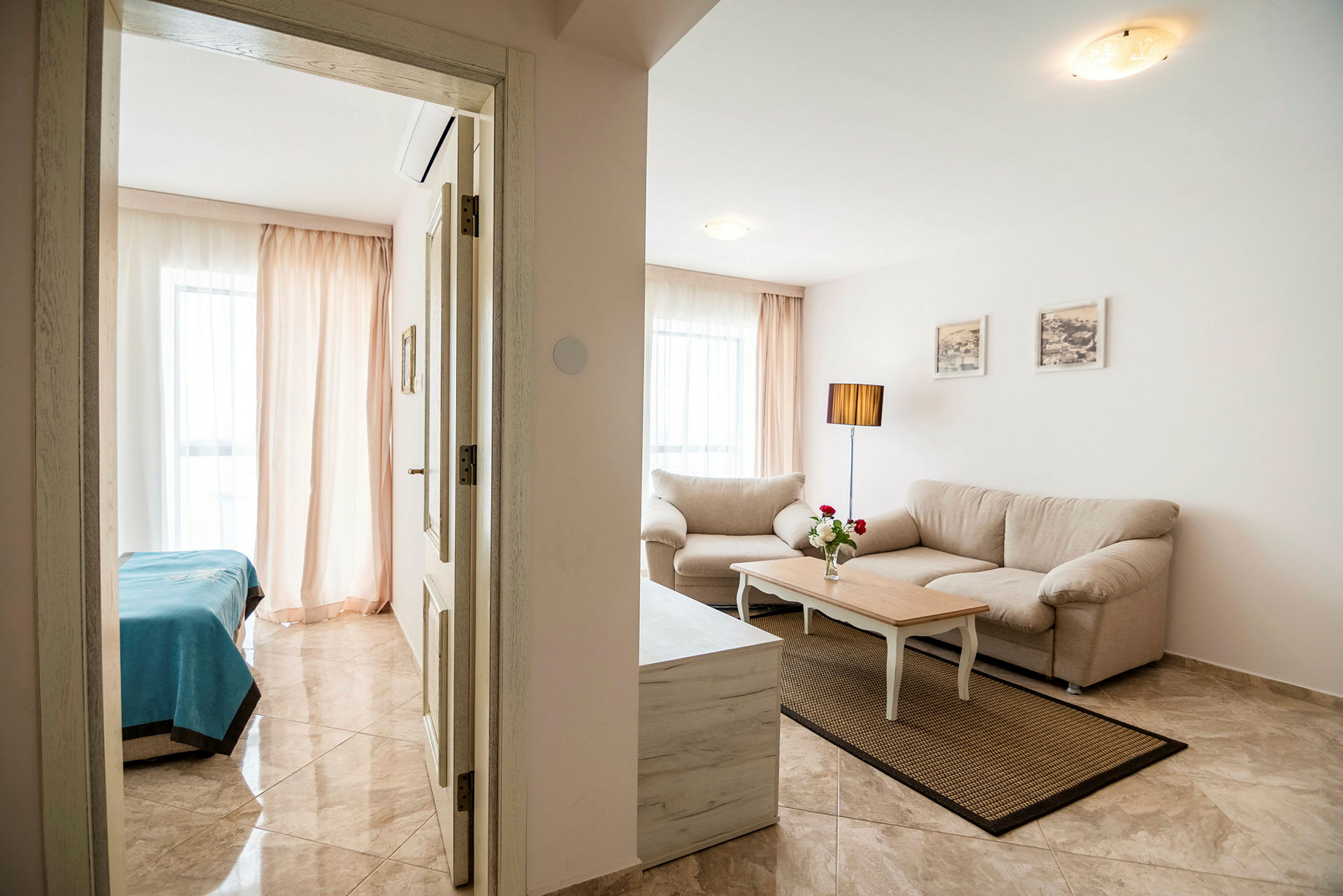 Interiør af en lys og stilren lejlighed med stue og soveværelse. I stuen er der en beige sofa, sofabord og en gulvlampe. (AI-genereret tekst)