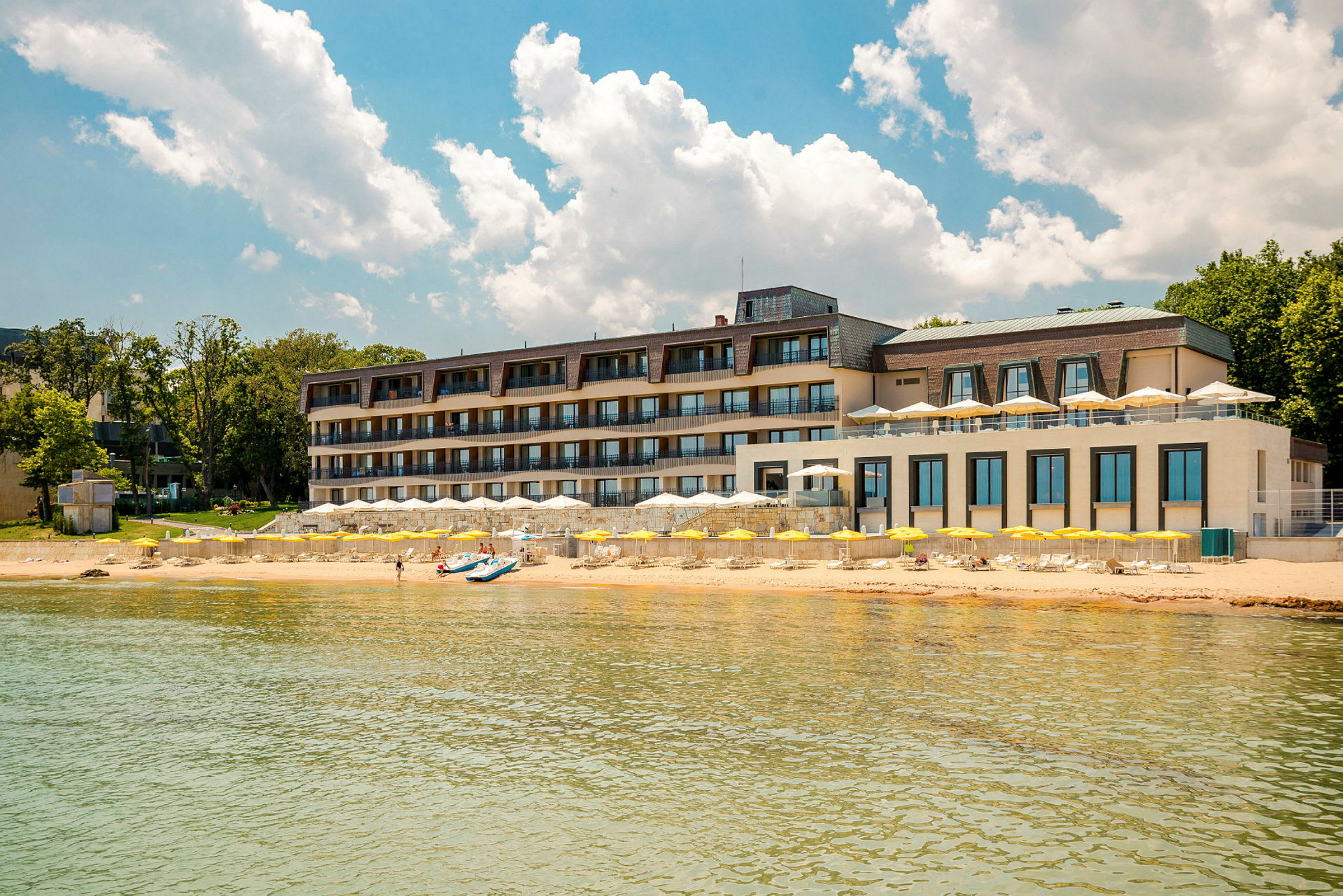 Fleretages hotel ved stranden med gule parasoller og klar blå himmel. (AI-genereret tekst)
