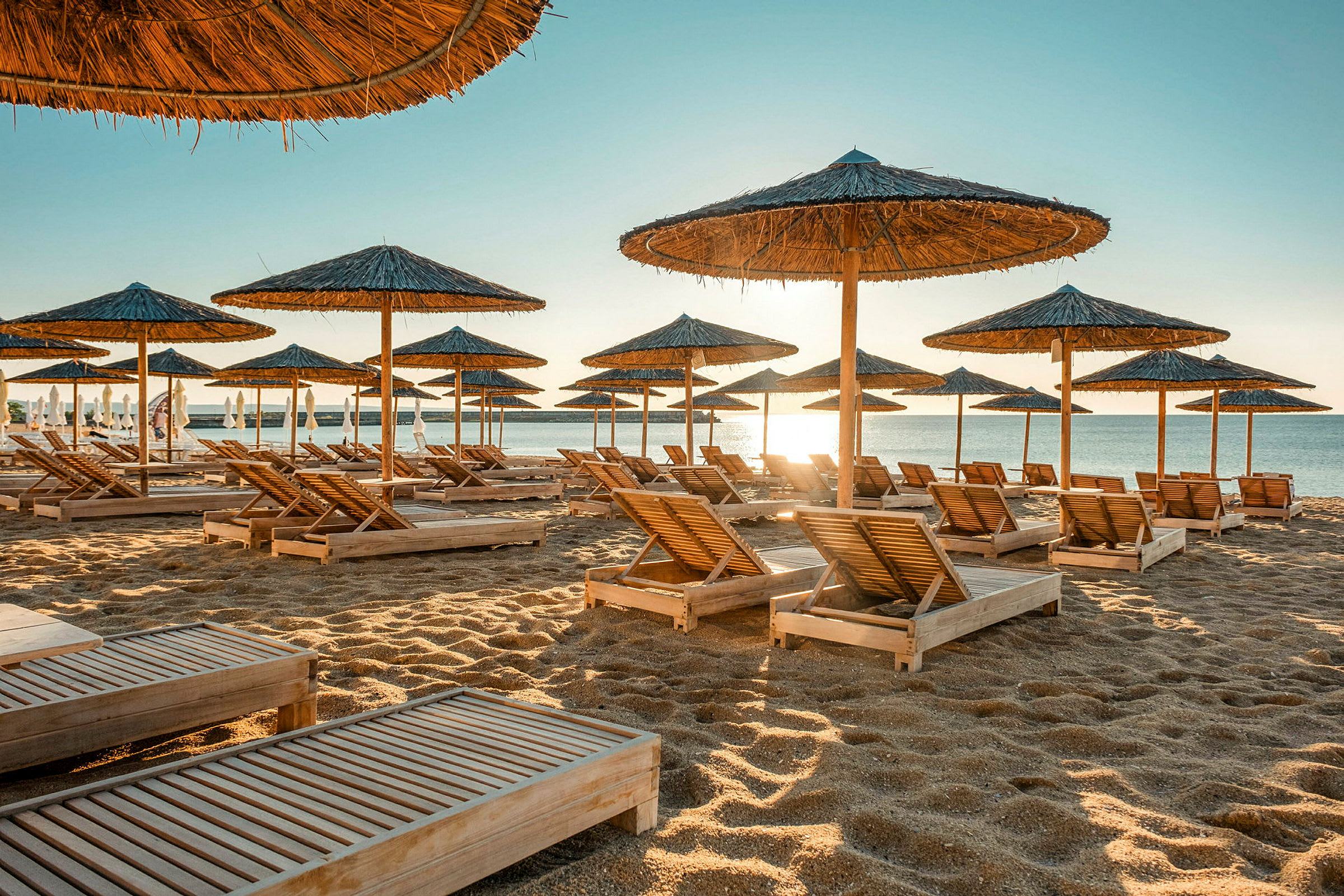 Strand med liggestole og parasoller af træ. (AI-genereret tekst)
