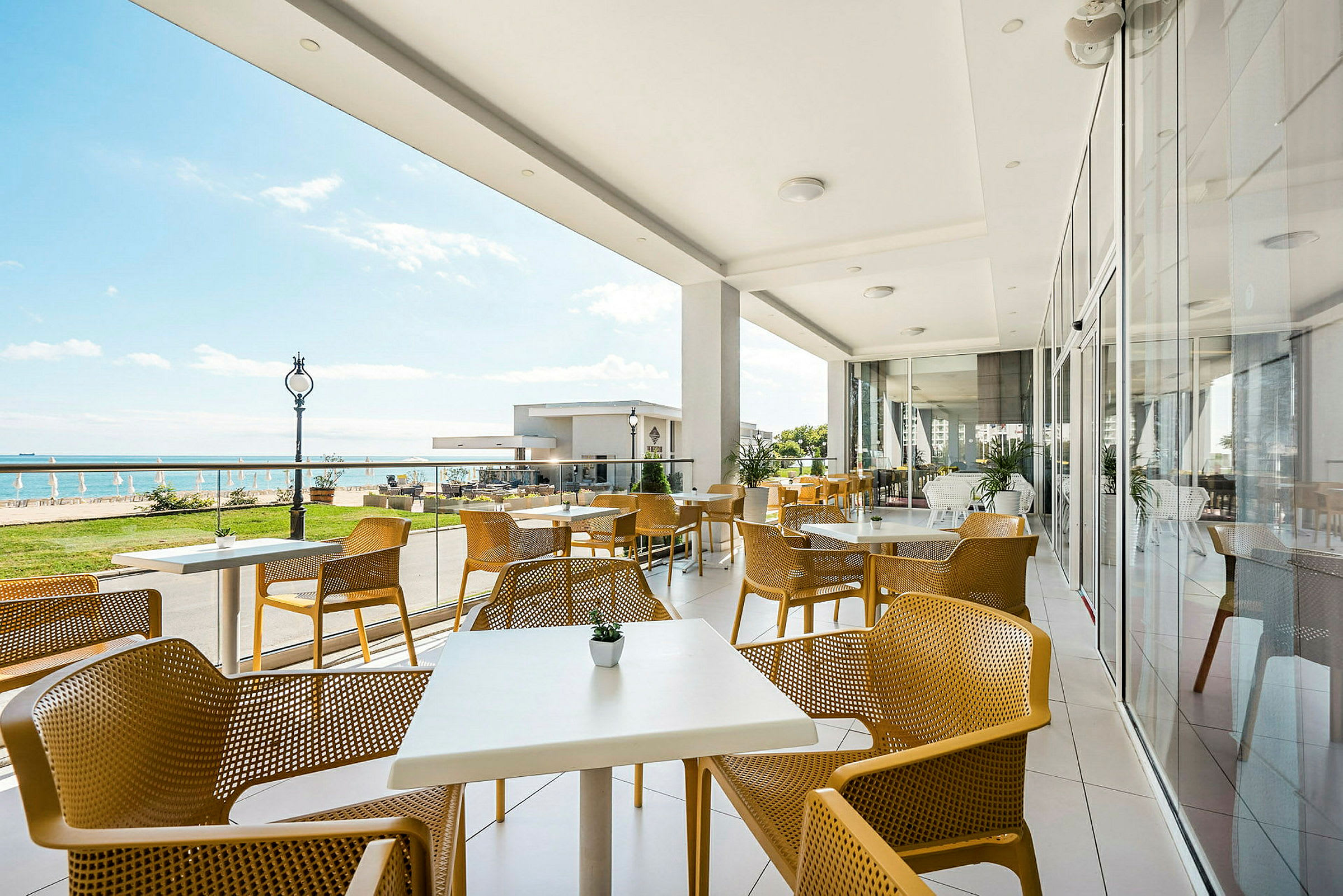 En udendørs terrasse med gule stole og hvide borde ved havet. (AI-genereret tekst)