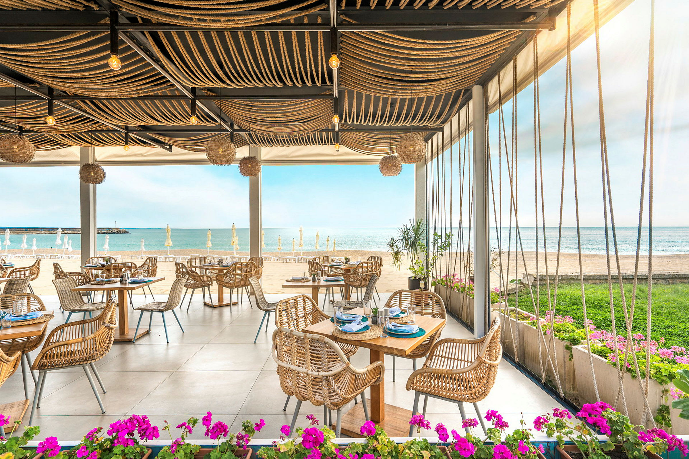 Restaurant ved stranden med udsigt over havet og borde med rottingstole. (AI-genereret tekst)