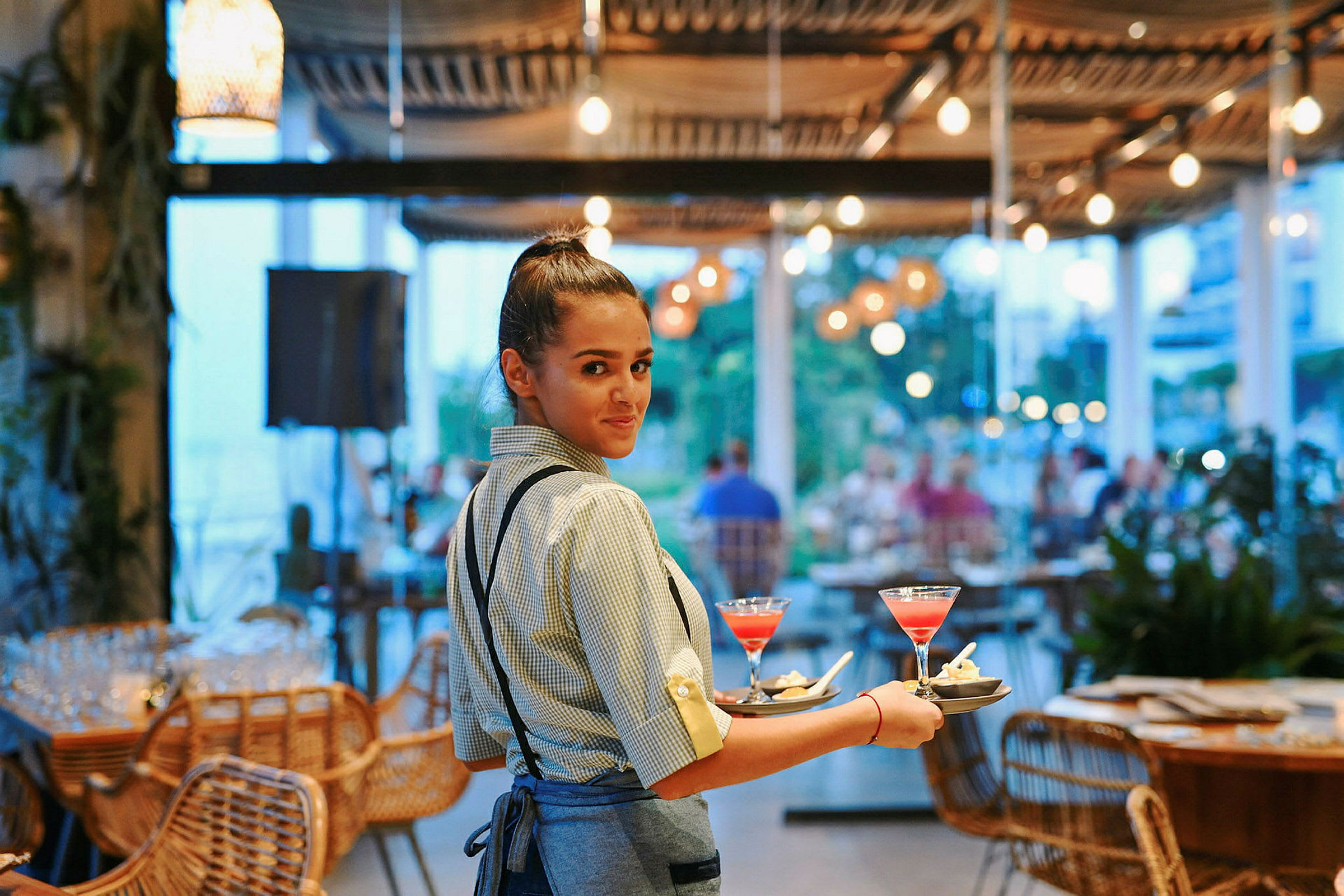 Tjener bærer bakker med farverige drikkevarer på en restaurant. (AI-genereret tekst)