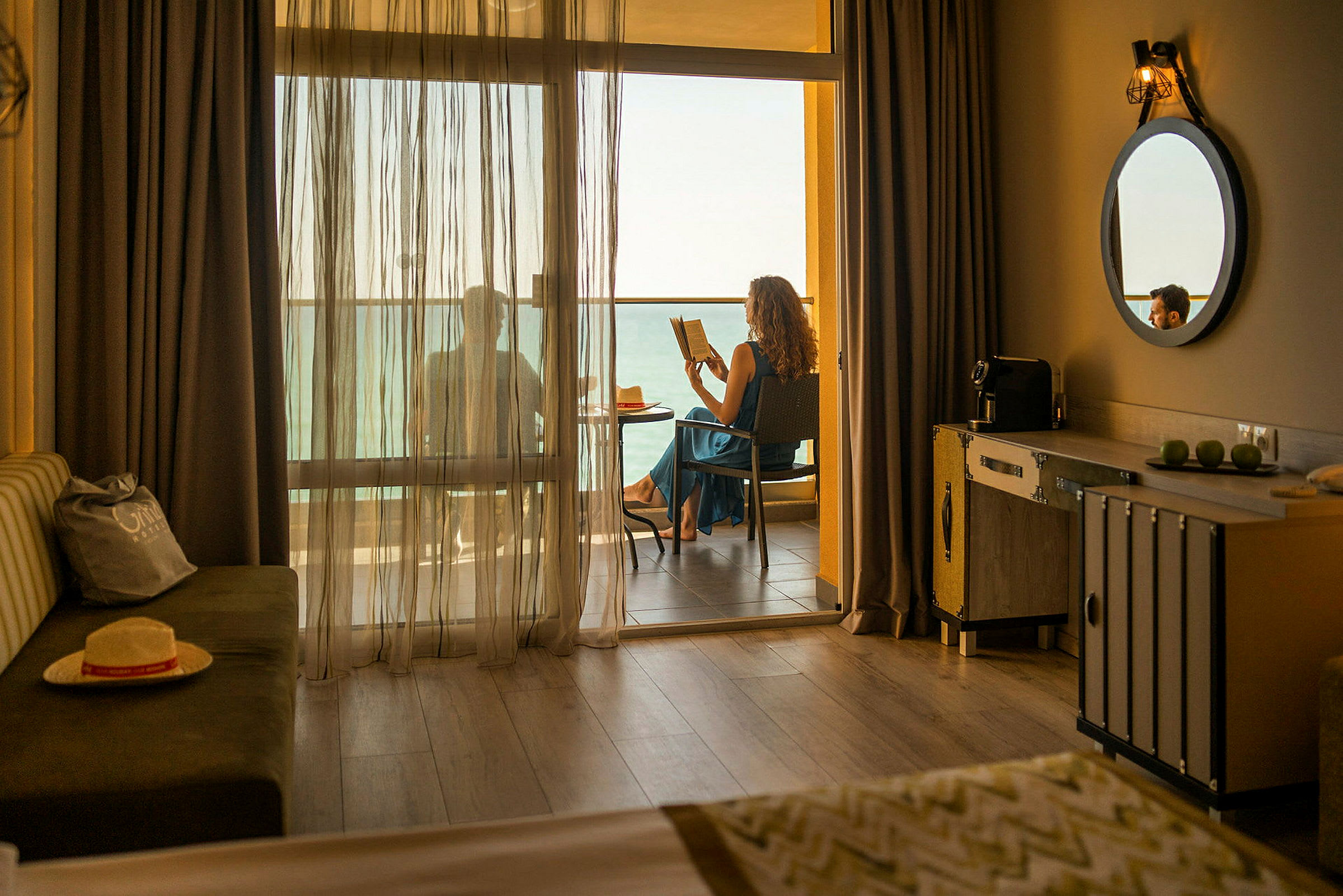 Hotelværelse med en altan, hvor en person sidder og læser med havudsigt. (AI-genereret tekst)