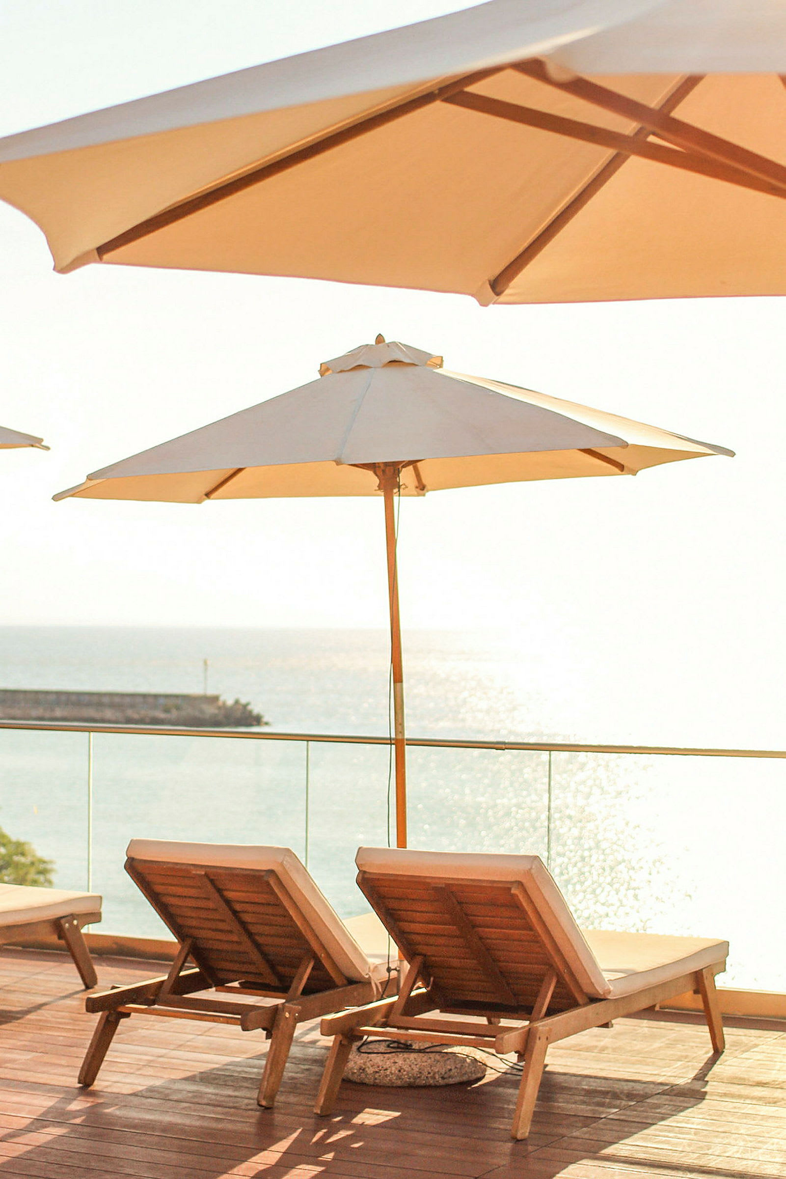 Liggestole med parasol på en terrasse med udsigt over havet. (AI-genereret tekst)