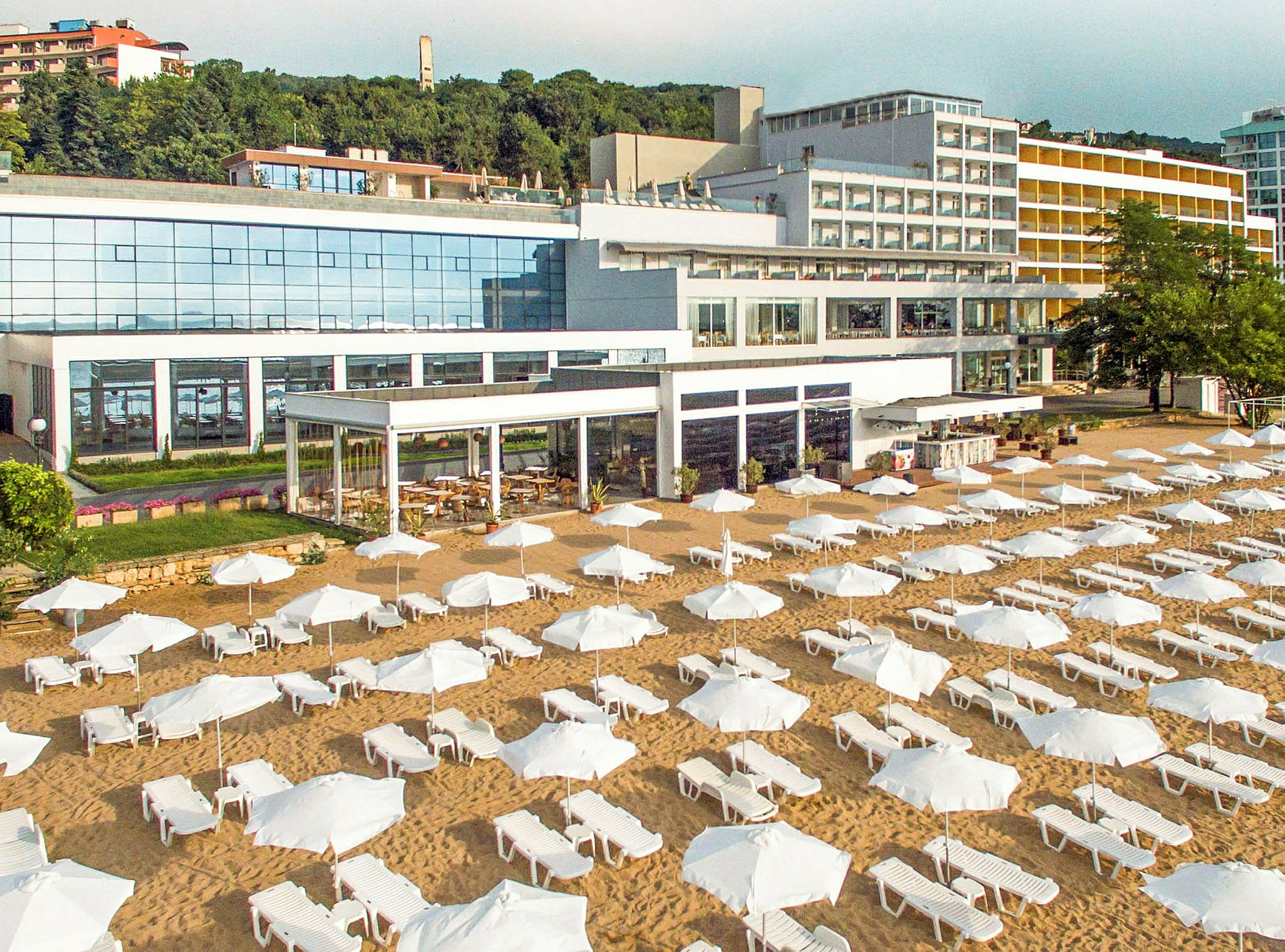 En strand med liggestole og parasoller foran et stort hotel. (AI-genereret tekst)