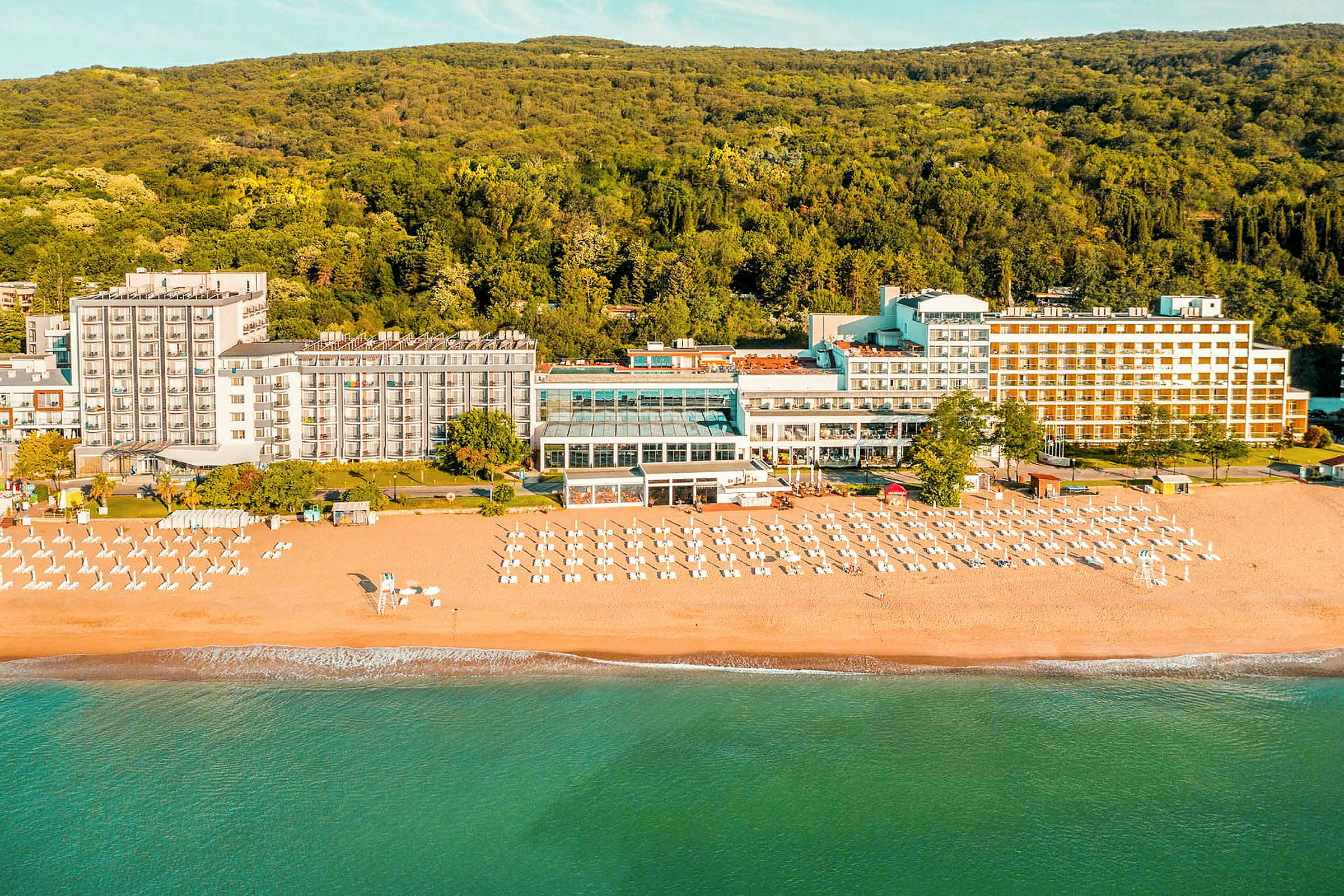 Hotel ved stranden med liggestole og parasoller foran en skov. (AI-genereret tekst)