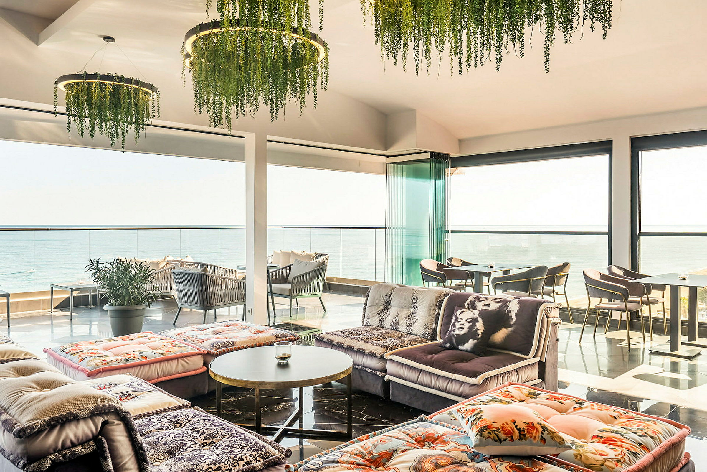 Et lyst indrettet rum med panoramaudsigt over havet, med sofaer og borde. (AI-genereret tekst)