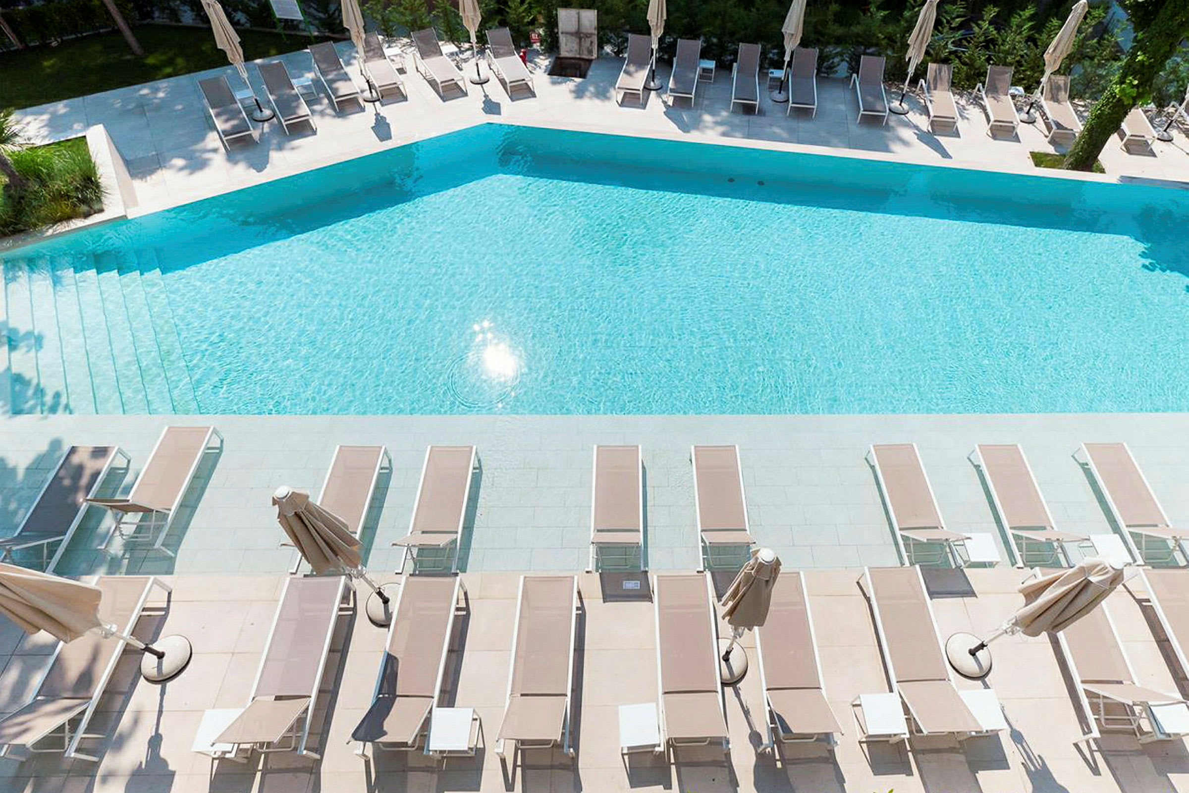 En swimmingpool med liggestole og parasoller ved siden. (AI-genereret tekst)