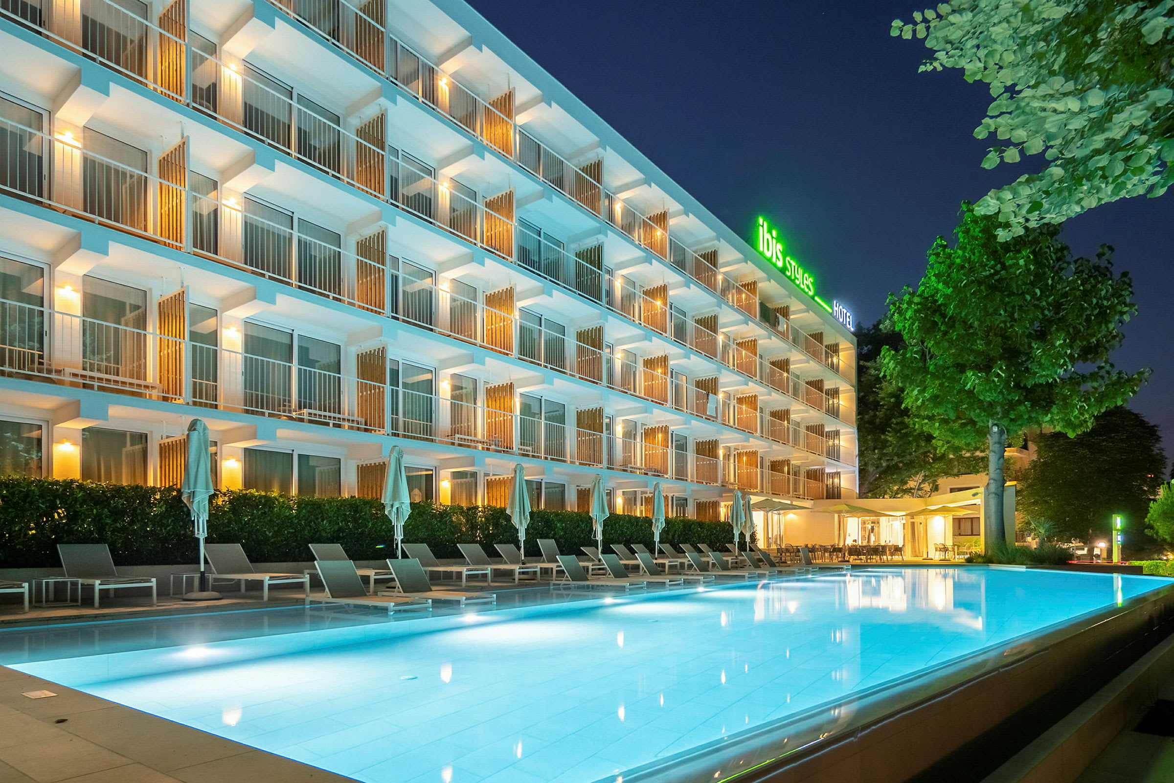 Hotel med udendørspool i moderne oplyst natstemning. (AI-genereret tekst)