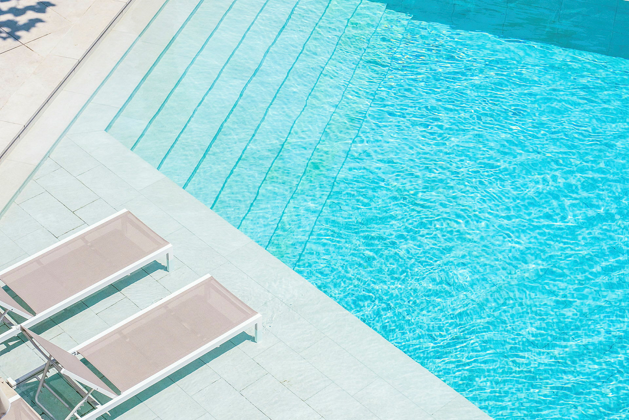 Lyse liggestole ved siden af en klart blå swimmingpool. (AI-genereret tekst)