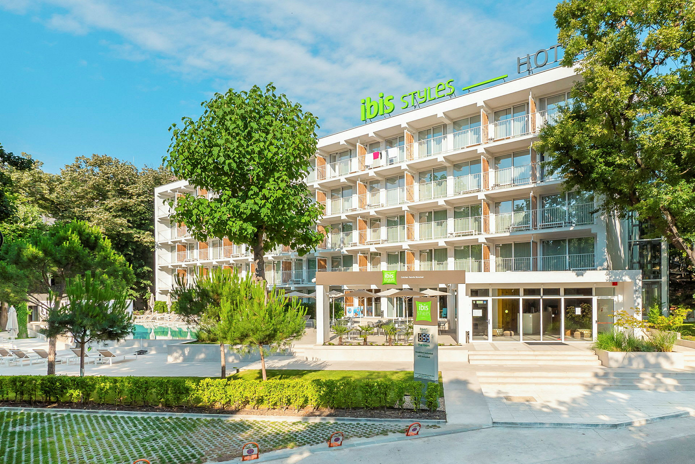 Moderne hotelbygning med flere etager, omgivet af grønne områder og træer. (AI-genereret tekst)