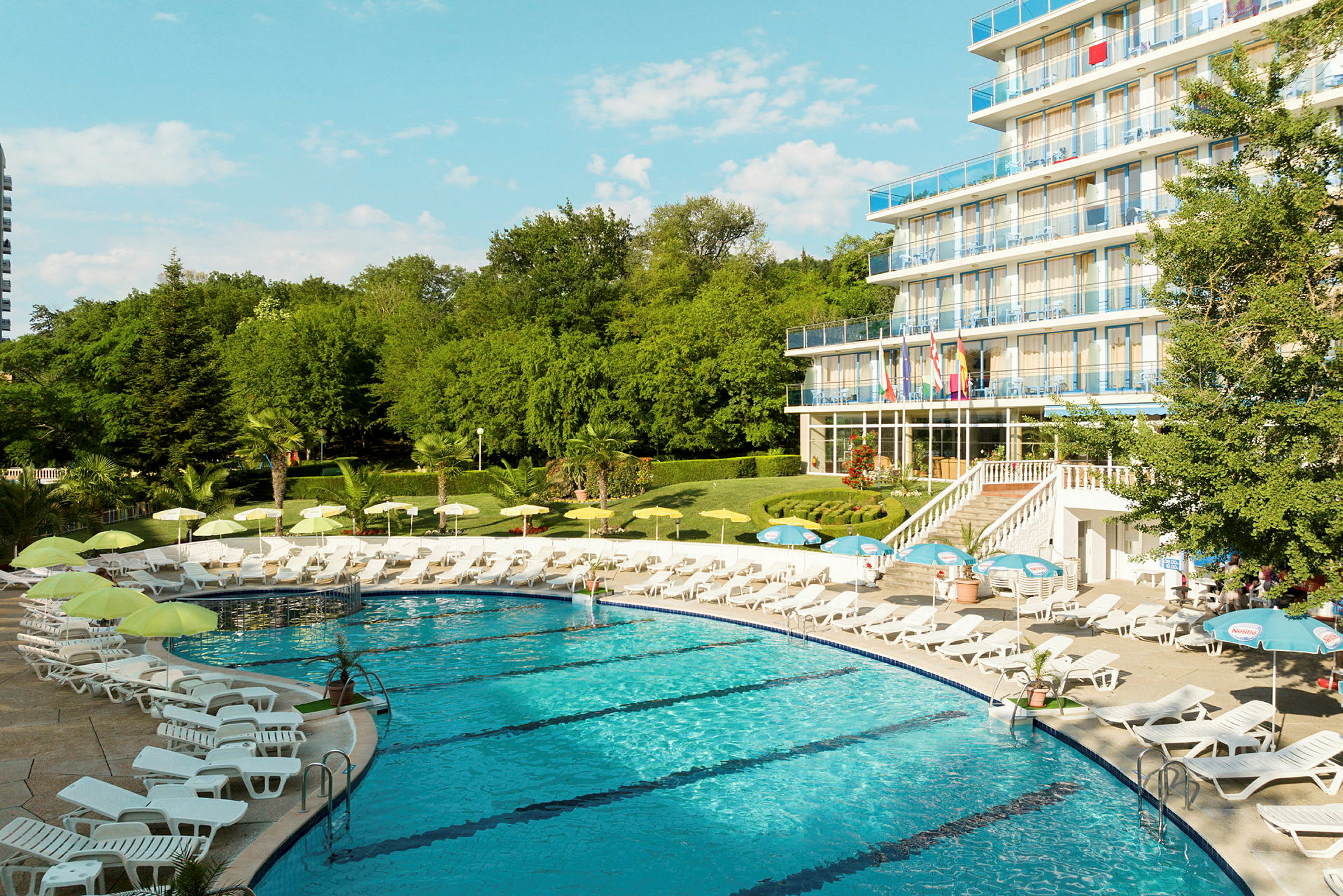 En pool omgivet af liggestole og parasoller nær et hotel med flere etager. (AI-genereret tekst)