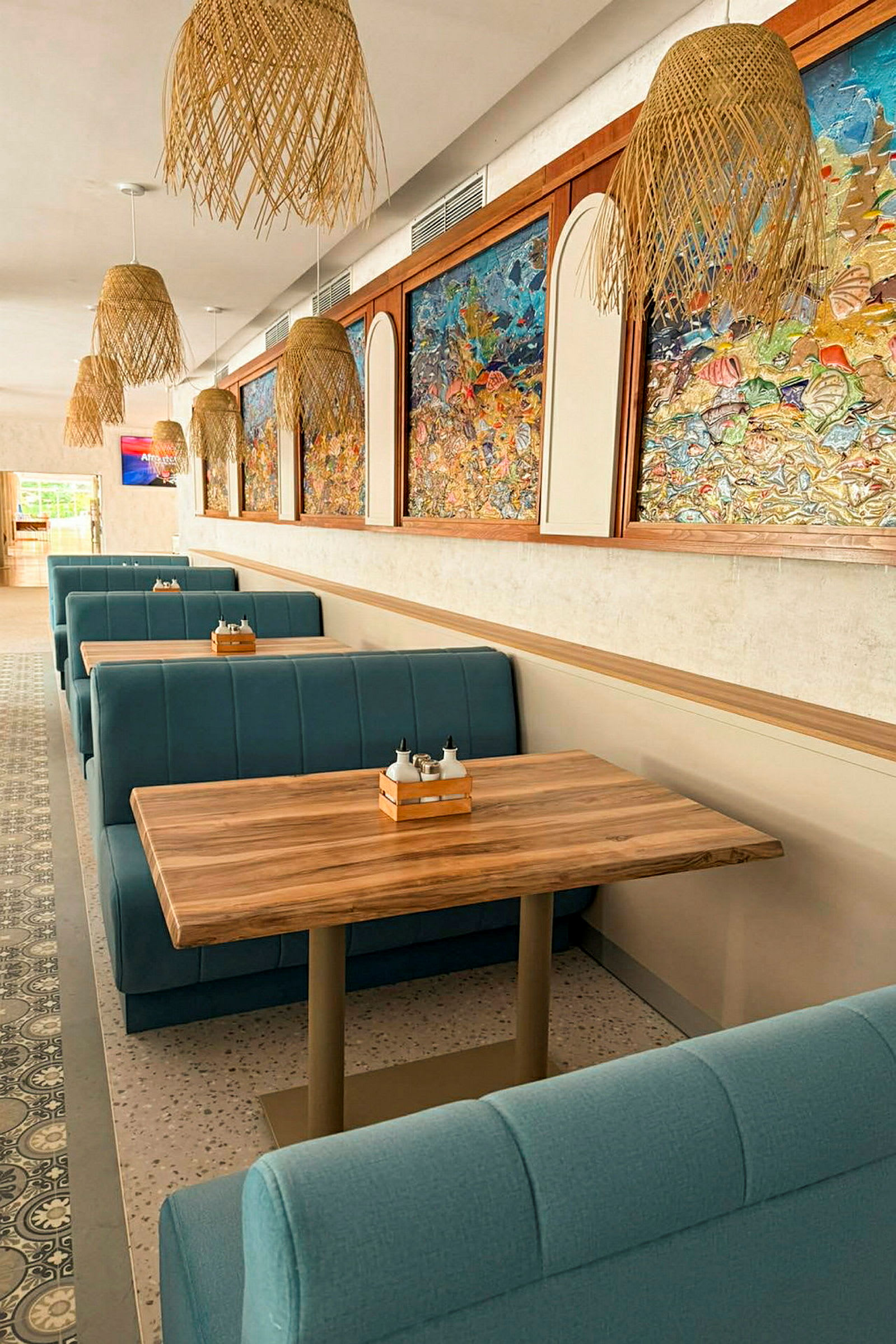 Billede af en restaurant med blå båse og træborde. Væggene er dekoreret med farverige kunstværker, og loftet har flettede lamper. (AI-genereret tekst)