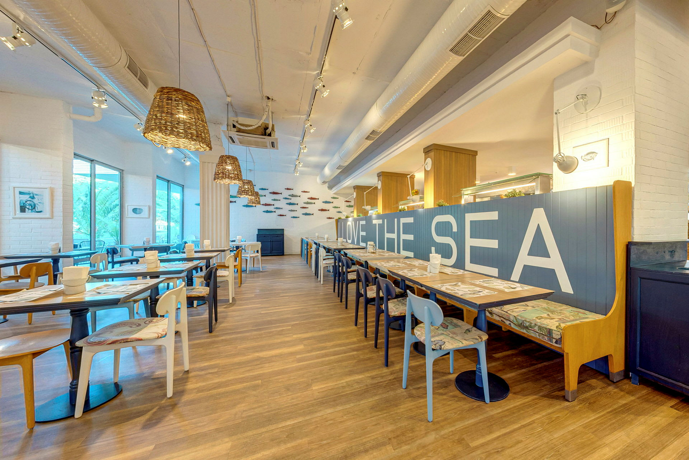 En moderne restaurant med lys indretning, træborde og stole samt teksten 'LOVE THE SEA' på en blå ryglæn. (AI-genereret tekst)