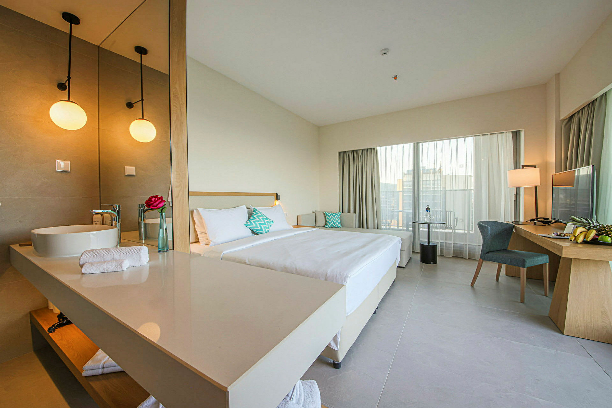 Et hotelværelse med en dobbeltseng, et skrivebord med stol og et stort spejl ved håndvasken. (AI-genereret tekst)