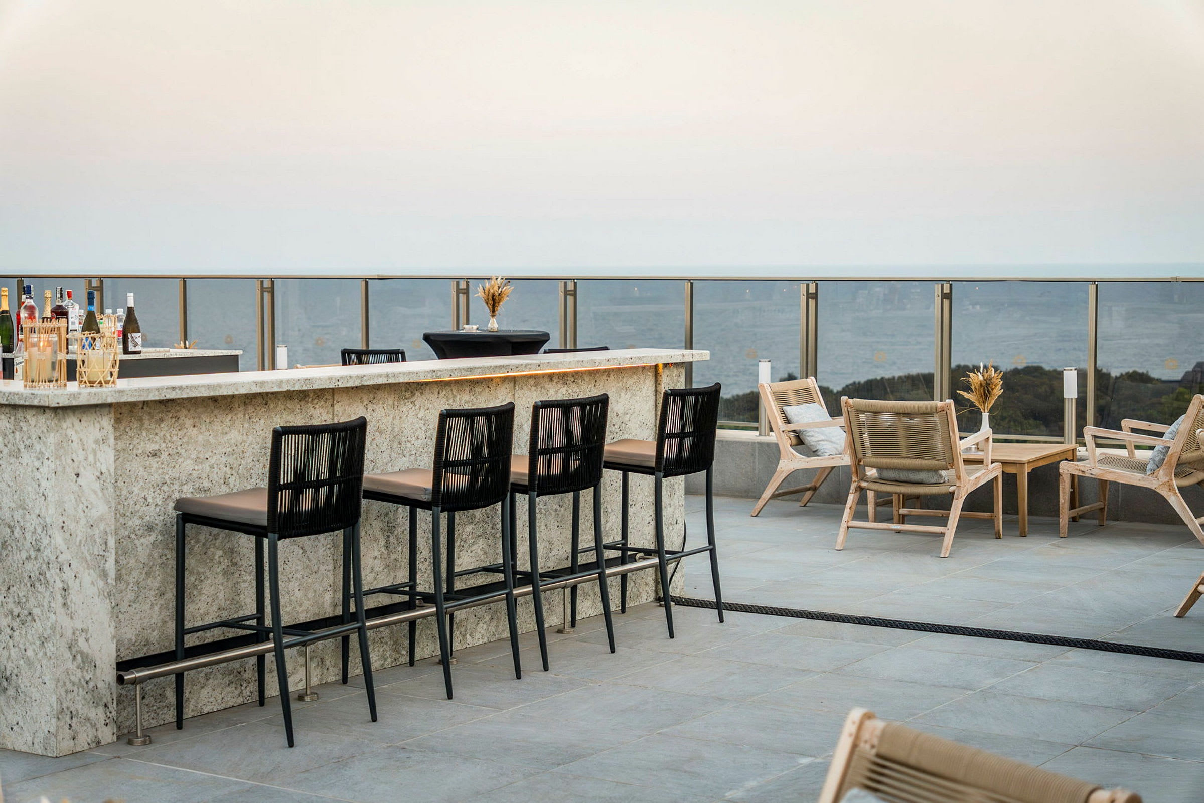 En udendørsbar med høje stole og loungemøbler på en terrasse med udsigt. (AI-genereret tekst)