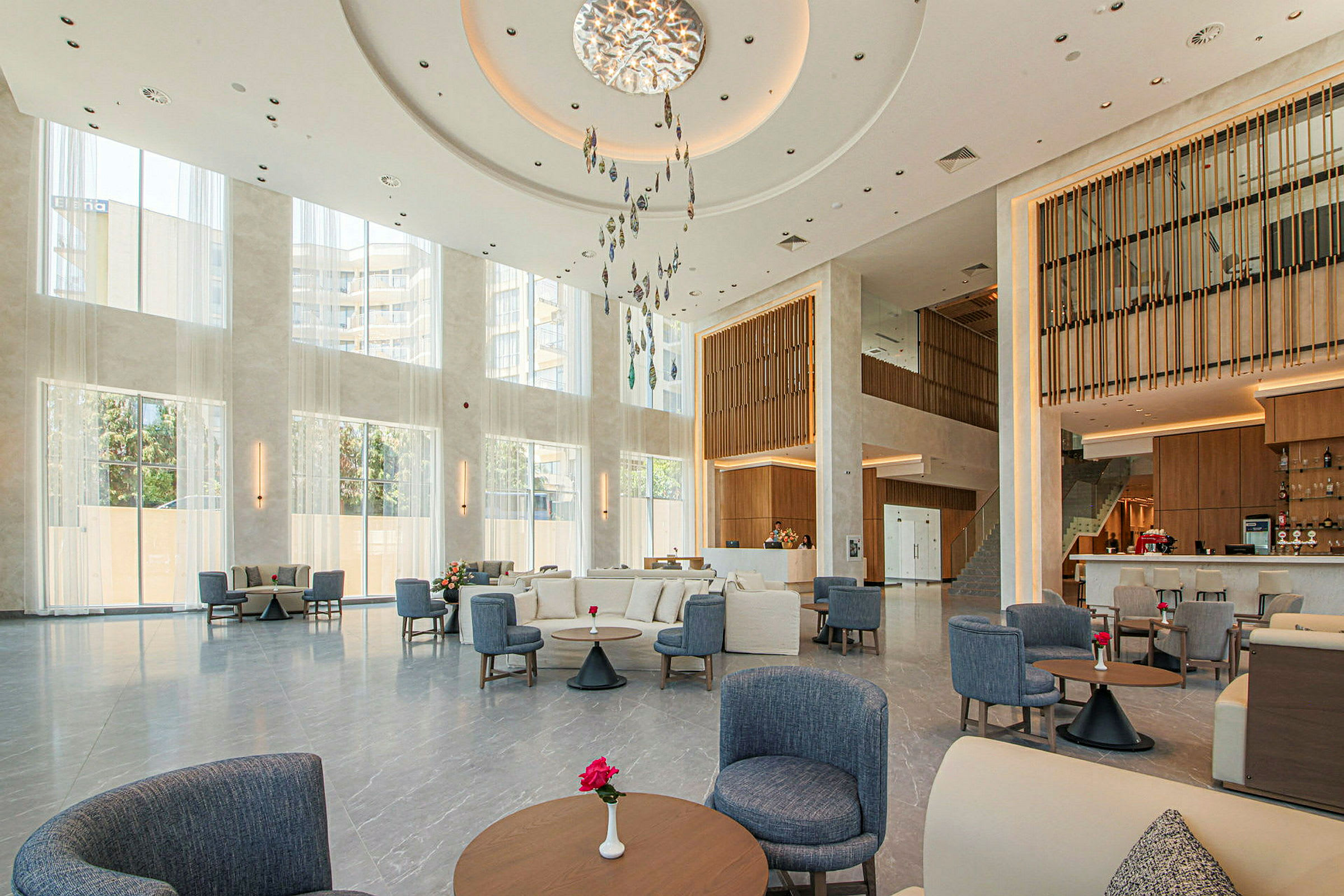 Billede af en lys hotellobby med store vinduer, moderne indretning og siddegrupper. (AI-genereret tekst)